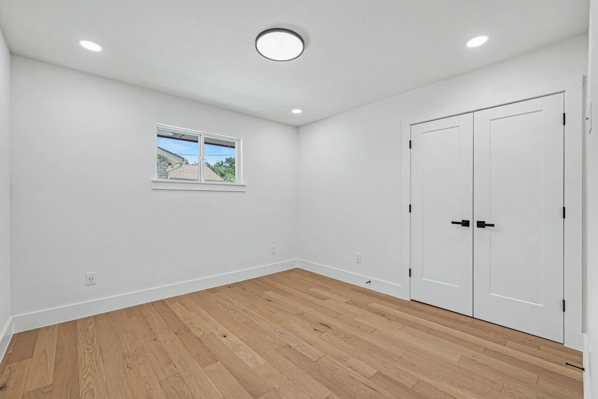 Recessed lighting, central ceiling light fixture, wood-finish flooring, white walls, and white double doors with matte black hardware