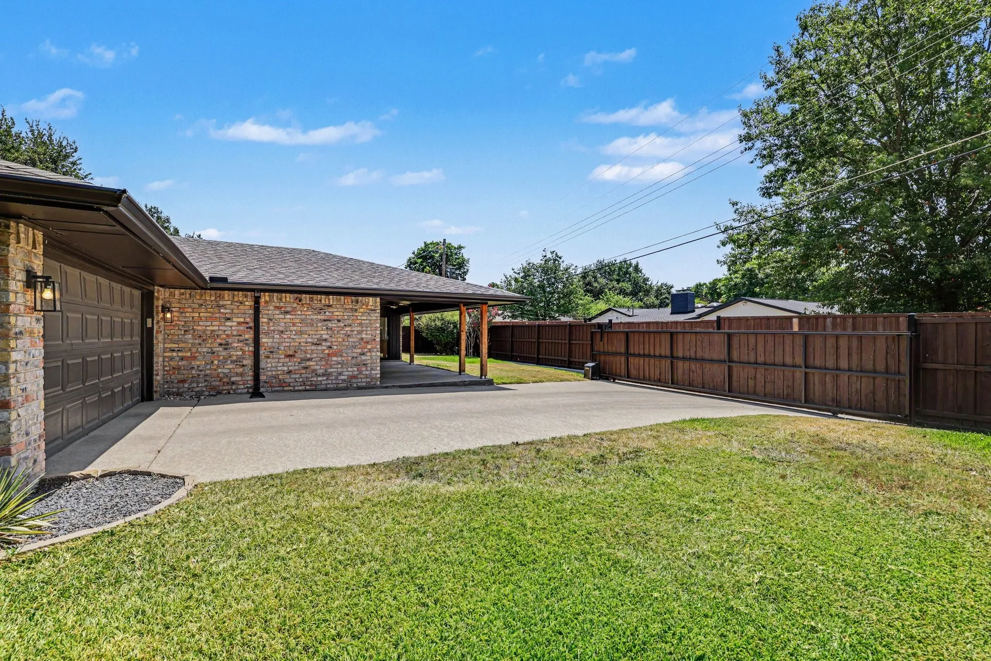 Brick exterior with attached garage, covered carport, concrete driveway, and wood privacy fencing