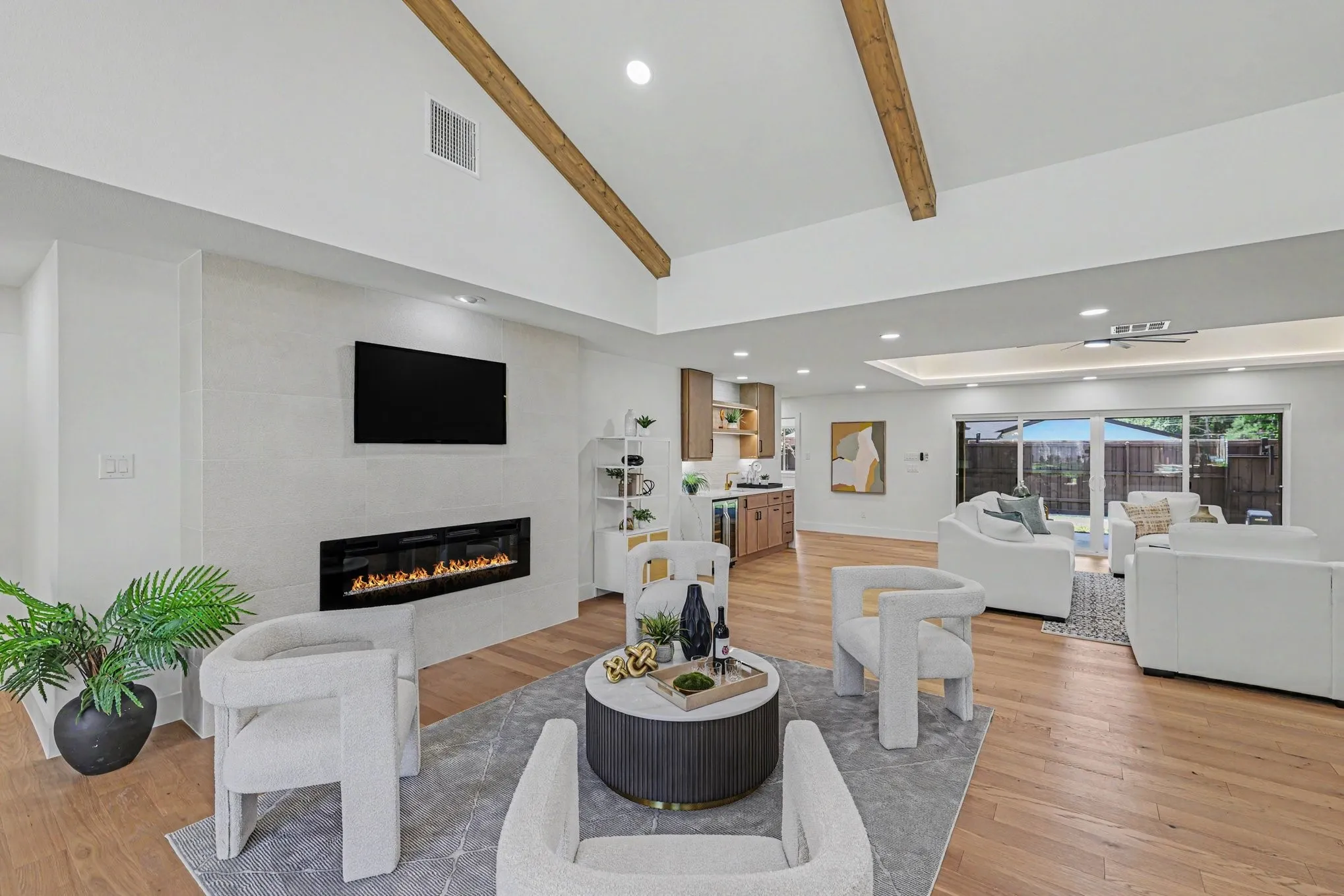 Vaulted ceiling with exposed wood beams, wood-finish flooring, built-in linear fireplace, recessed lighting, and sliding glass doors