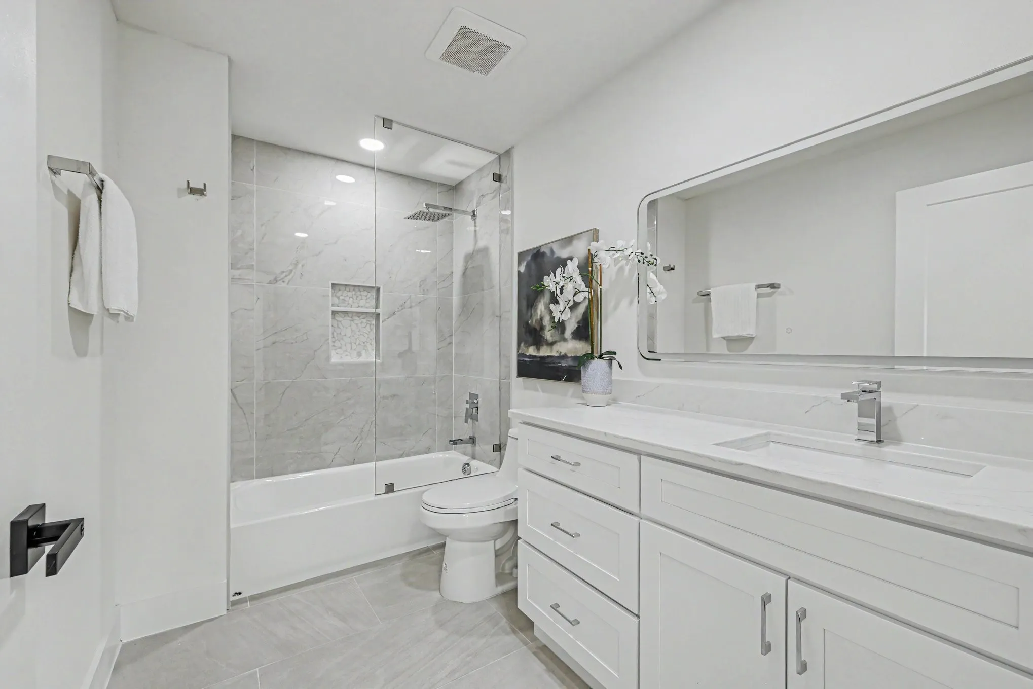 Tiled shower with glass enclosure and recessed niches, dual vanity with undermount sinks, and a large mirrored cabinet