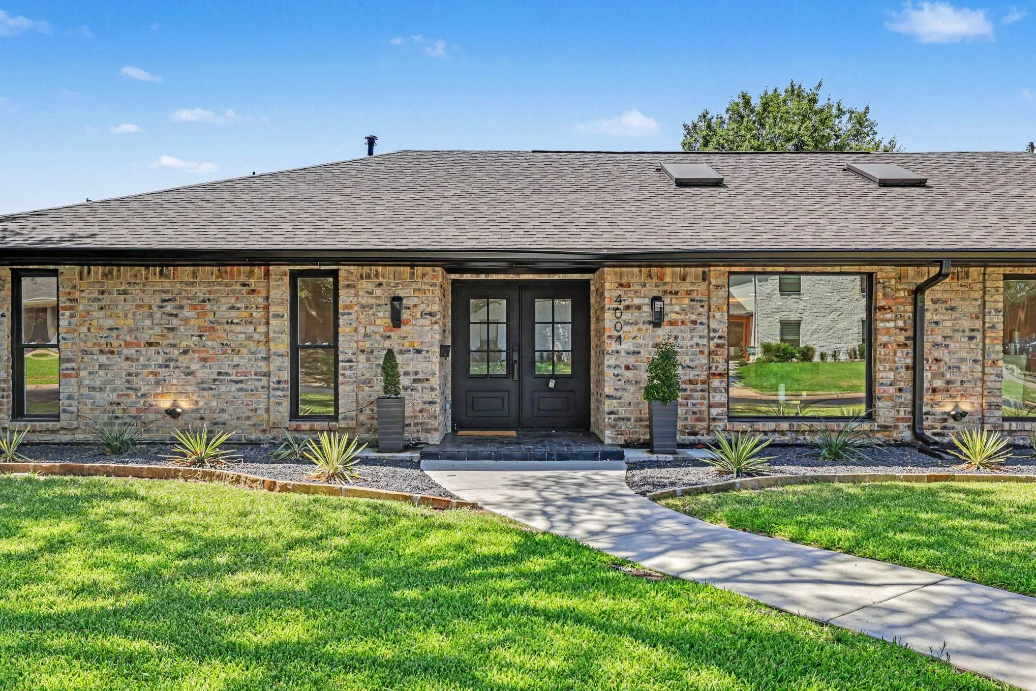 Brick exterior with dark-framed windows, double entry doors, and a shingle roof