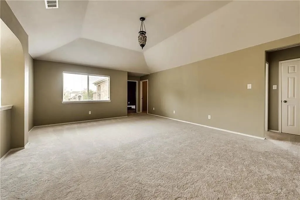Vaulted ceiling with an ornate pendant light fixture, soft carpet flooring, and a large window