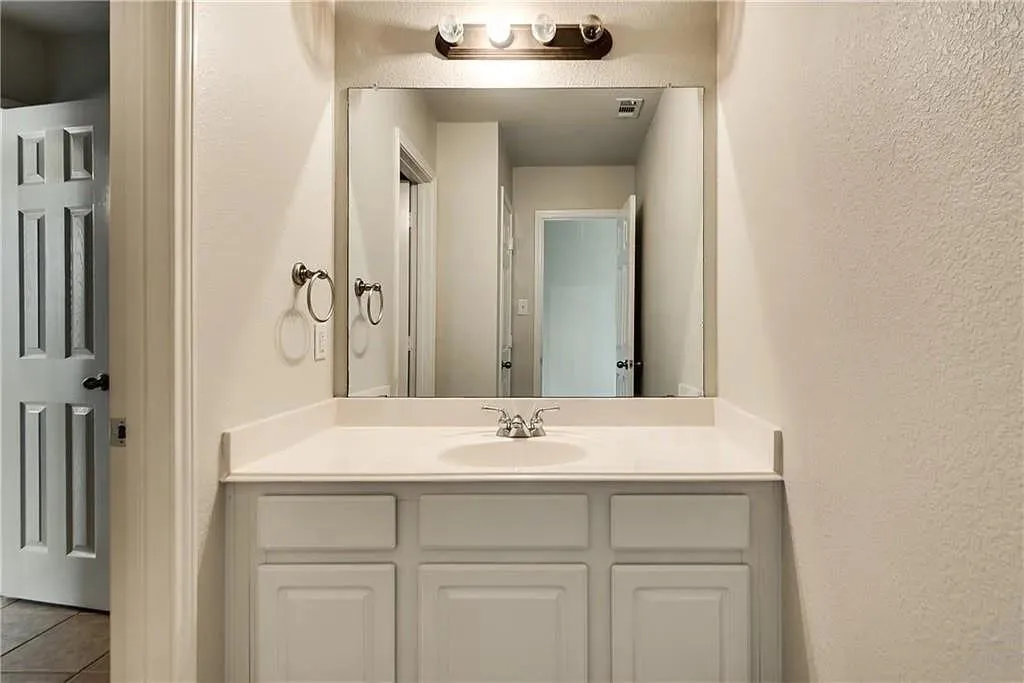 Vanity featuring a white countertop with an integrated sink, a large wall-mounted mirror, and a three-light fixture