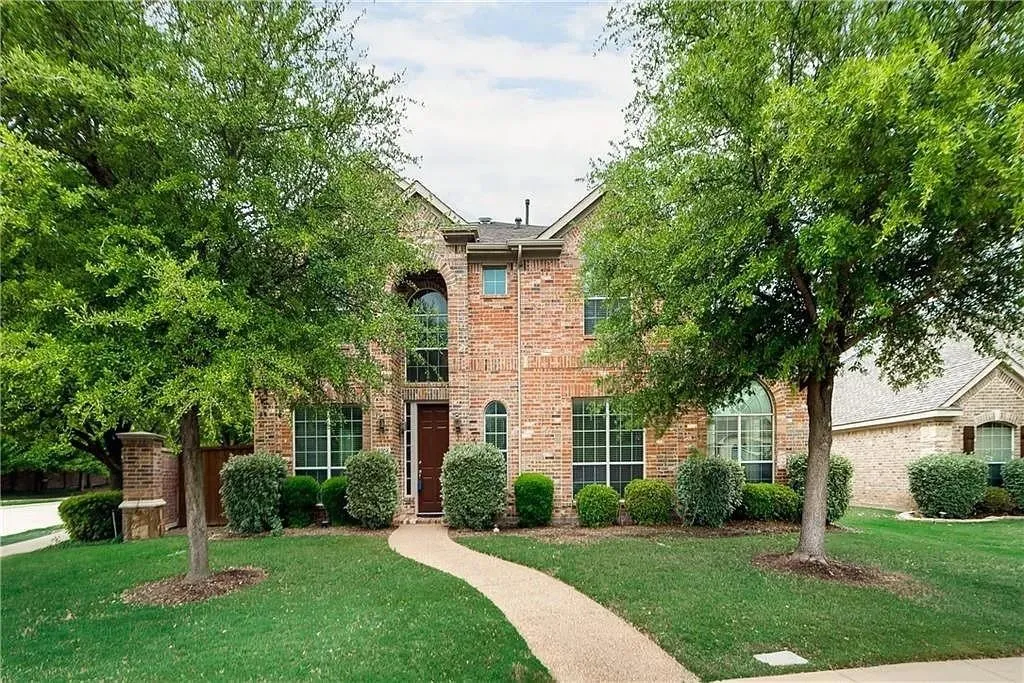 Brick exterior featuring arched windows, mature landscaping, a curved walkway, and a prominent front entry