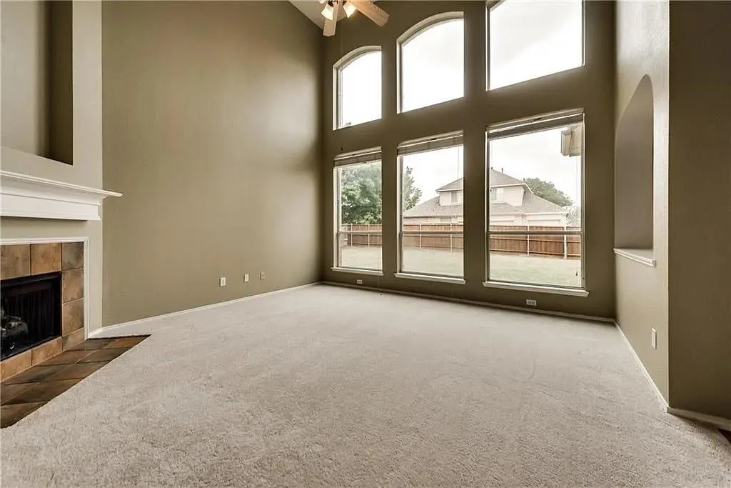 Vaulted ceiling with ceiling fan, large arched windows, tile-surround fireplace with mantel, and carpeted flooring