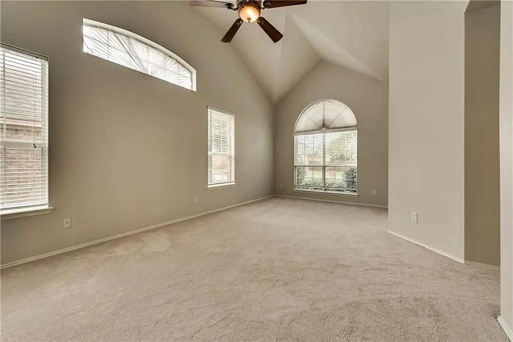 Vaulted ceiling with a ceiling fan, arched windows, rectangular windows with blinds, and neutral carpet flooring