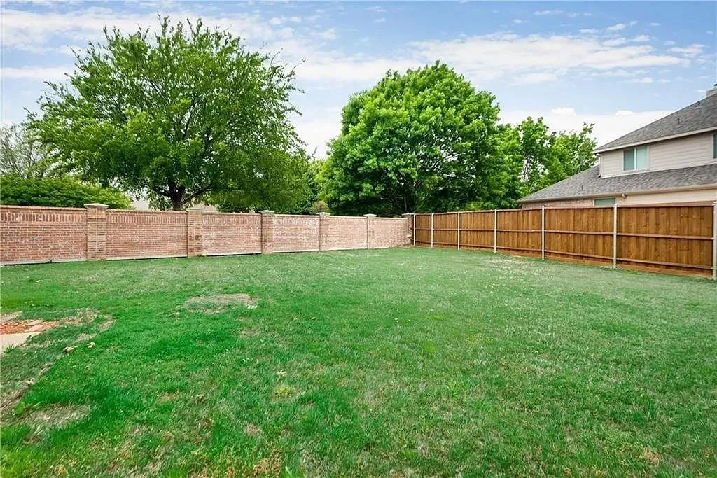 Expansive grassy yard with a brick perimeter wall, wood privacy fence, and mature trees