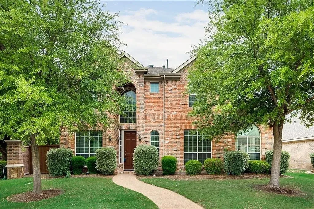 Brick exterior with an arched entry window, a covered entryway, mature trees, manicured landscaping, and a winding pathway