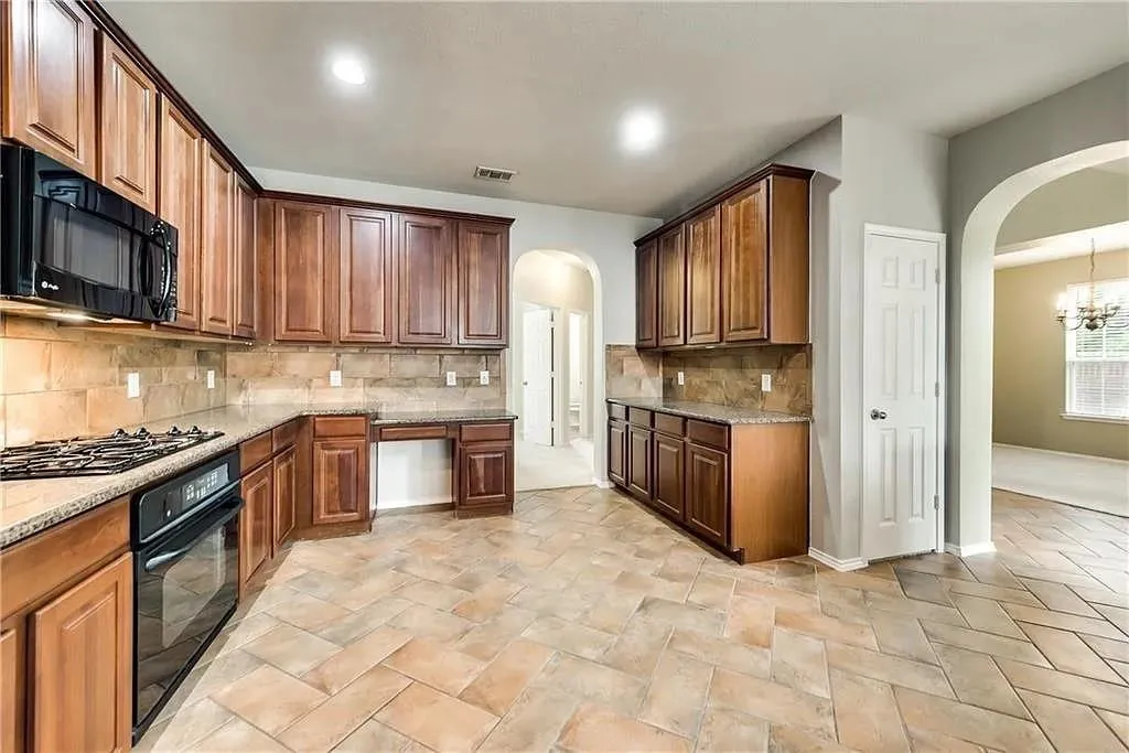 Tile flooring in a herringbone pattern, extensive wood cabinetry, built-in microwave, gas cooktop, and arched doorways
