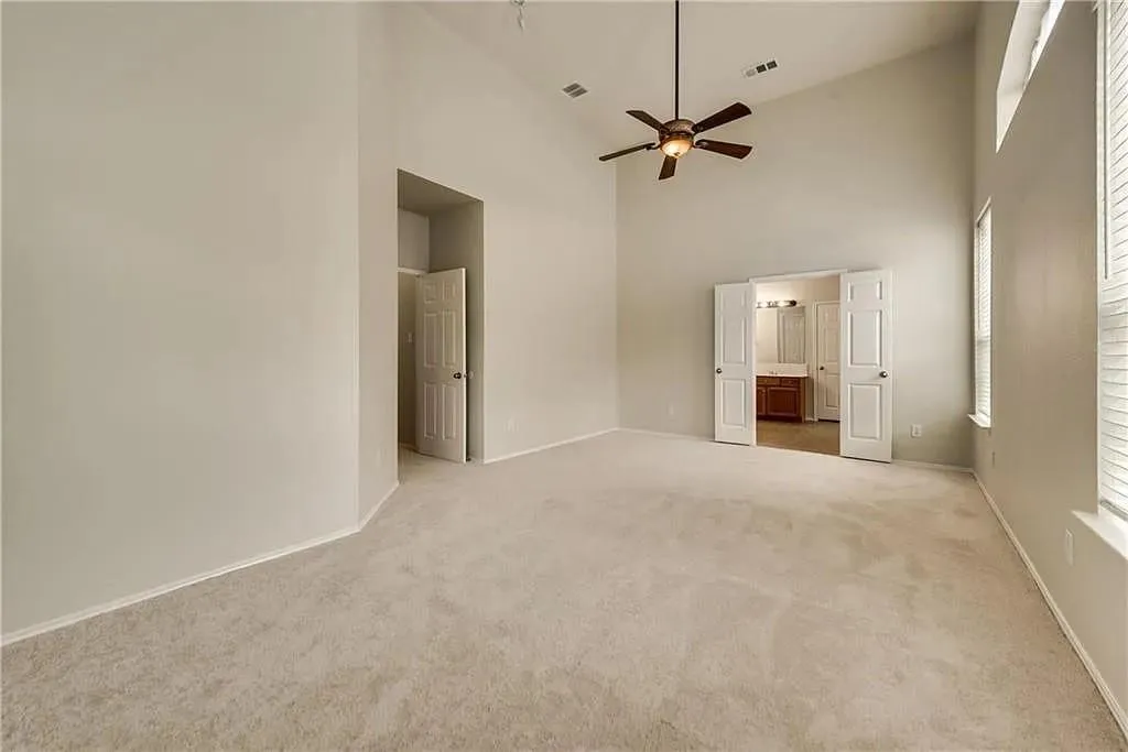Vaulted ceiling, ceiling fan with integrated lighting, neutral carpet, double windows with blinds, and white panel doors