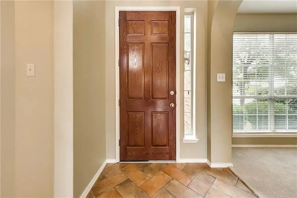 Wood-paneled entry door with sidelight, terra cotta-toned tile flooring, and arched doorway