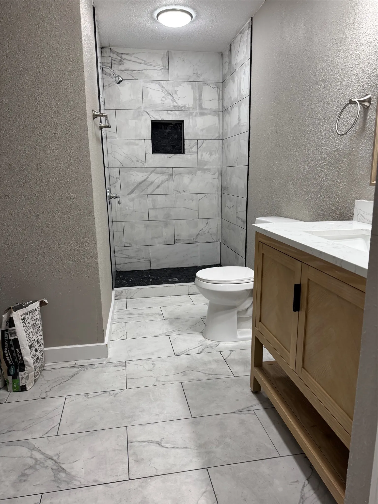 Modern bathroom featuring a glass-enclosed shower with white tiled walls and a dark tiled shower floor, a white toilet, a light wood-finish vanity with a white countertop, and large format tiled flooring
