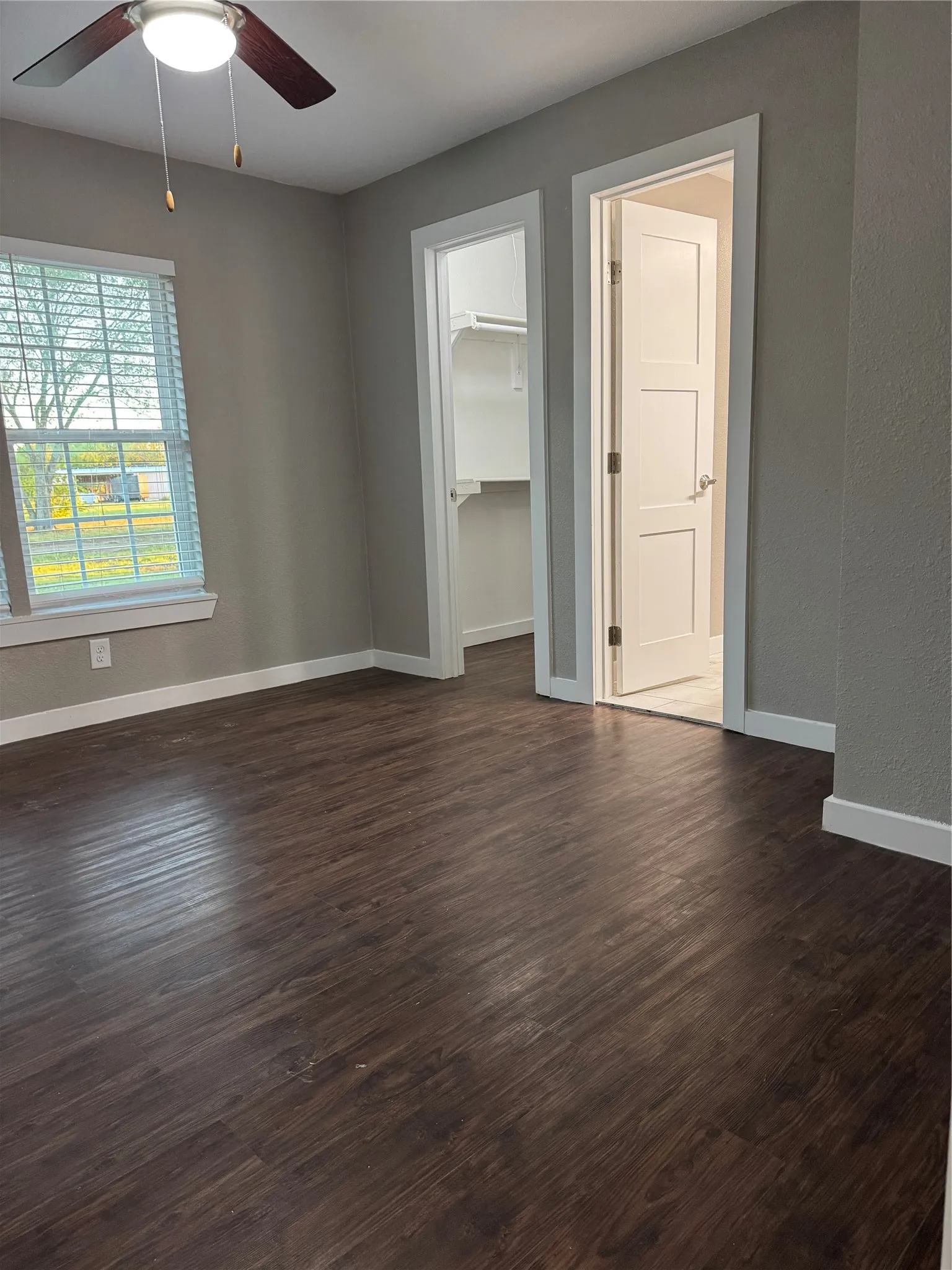 Wood-finish flooring, ceiling fan with integrated lighting, window with blinds, and a built-in closet with shelving