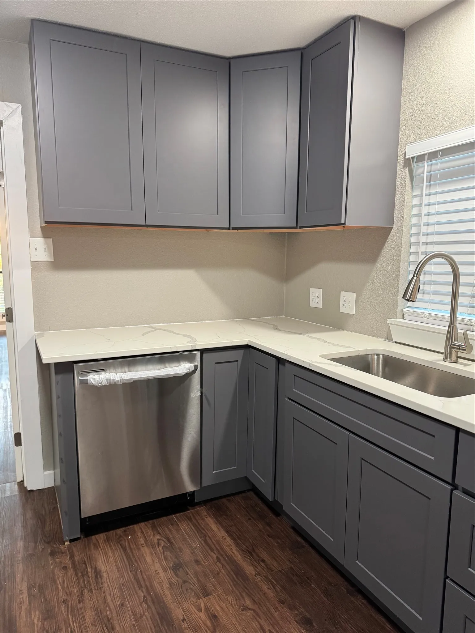 Modern kitchen featuring gray shaker-style cabinetry, light-toned countertops, a stainless steel dishwasher, an undermount stainless steel sink, and wood-finish flooring