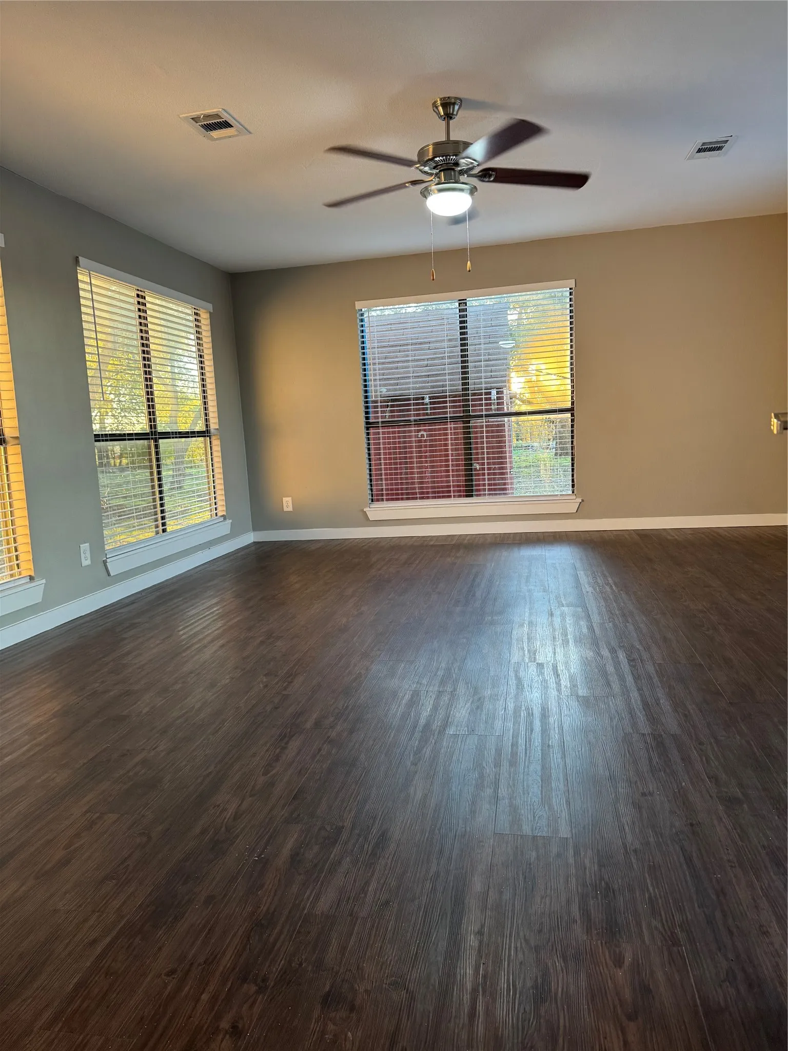 Spacious room featuring wood-finish flooring, multiple windows, a ceiling fan with integrated lighting, and neutral wall tones
