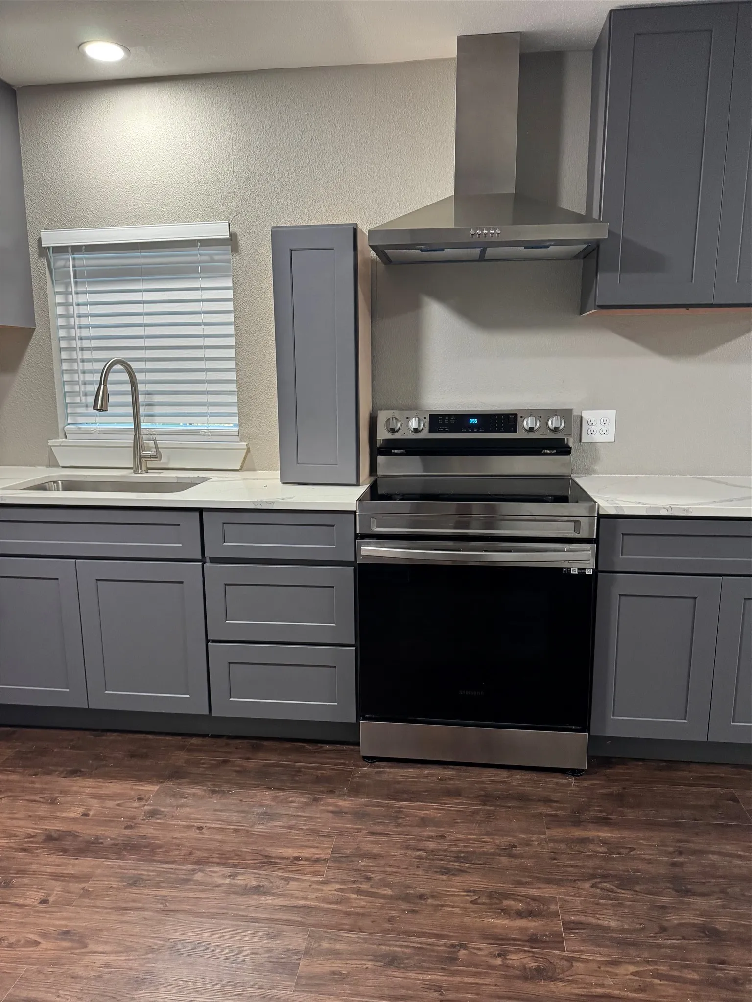 Gray shaker-style cabinetry with white countertops, wood-finish flooring, a stainless steel range, and a stainless steel range hood