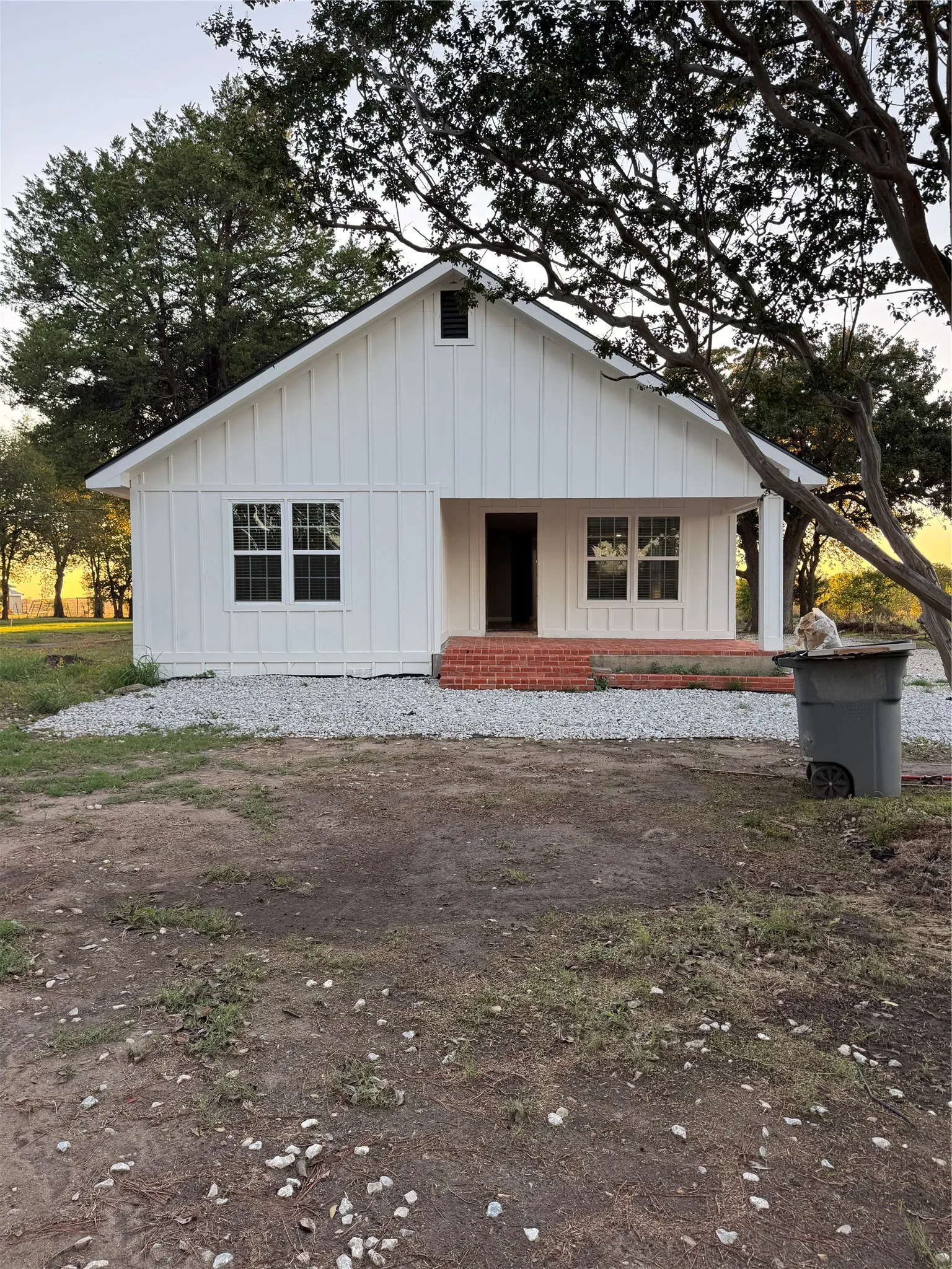 White board and batten siding, brick porch with white columns, gabled roofline, and multiple pane windows