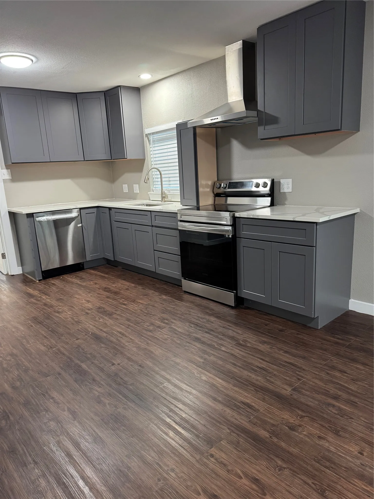 Contemporary kitchen featuring dark wood-finish flooring, grey cabinetry, stainless steel appliances, and light-toned countertops