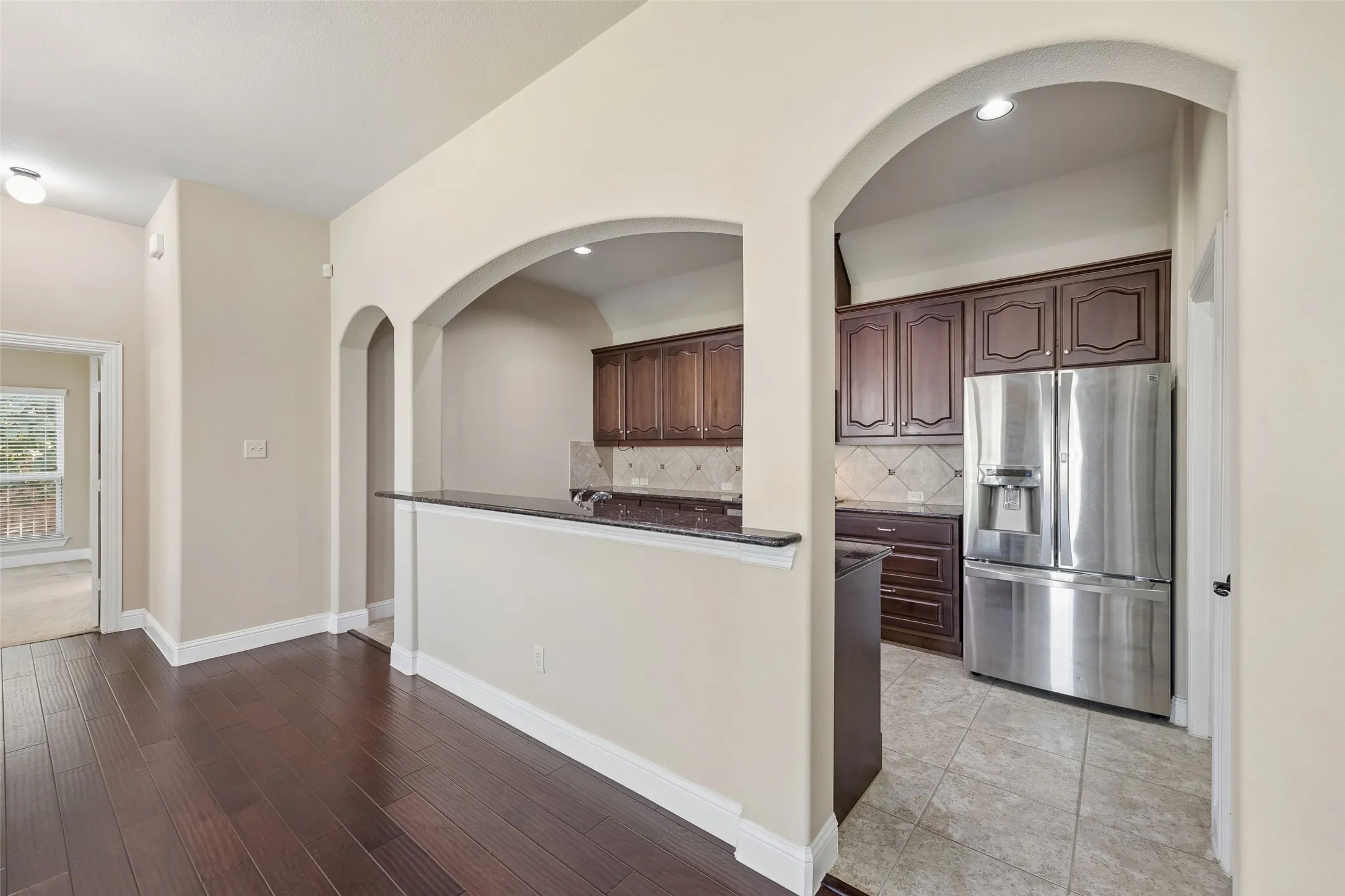 Dark wood-finish flooring, arched doorways, a breakfast bar with a dark countertop, stainless steel refrigerator, and dark wood cabinetry