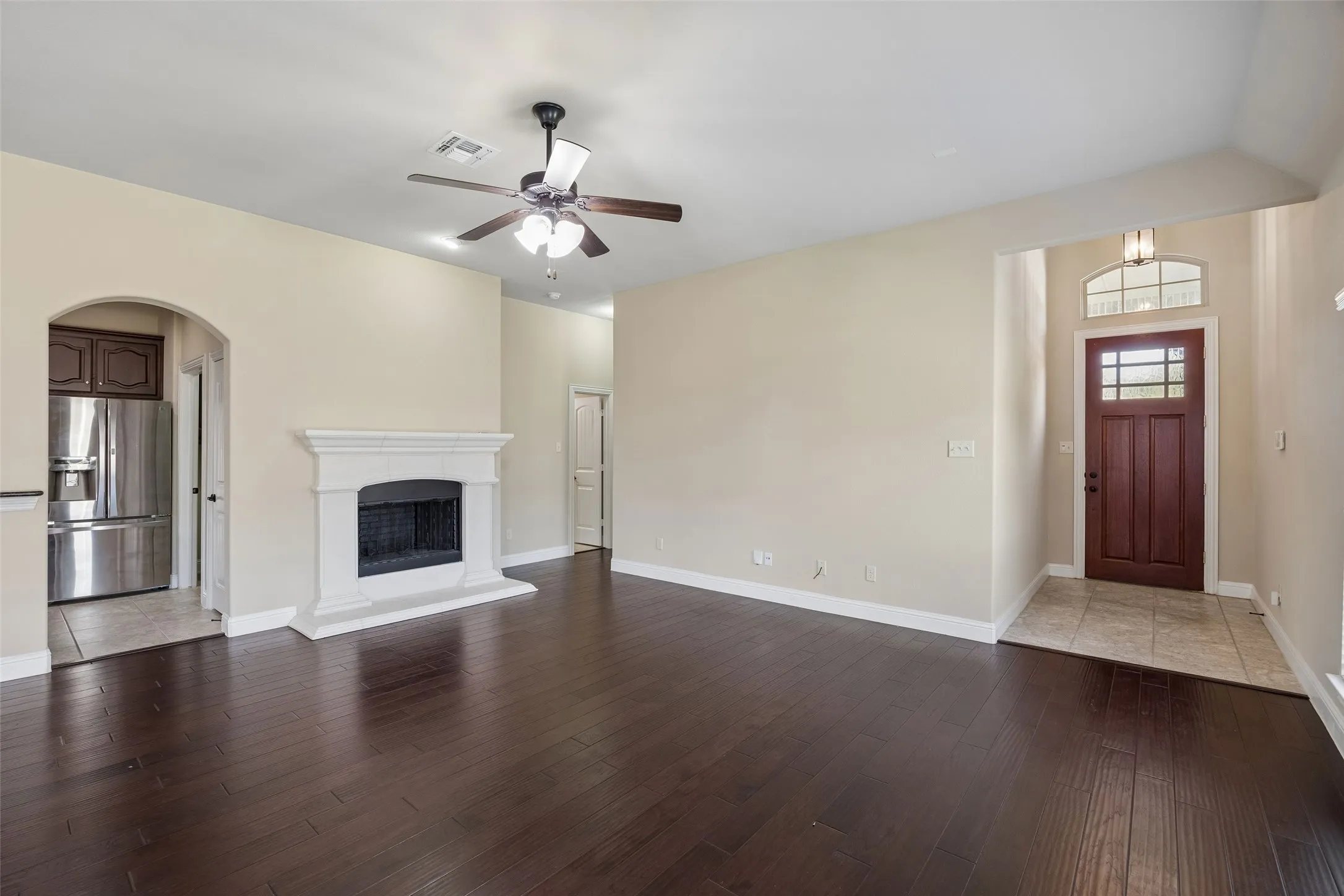 Spacious living area featuring dark engineered wood flooring, a white mantel gas fireplace, and a ceiling fan
