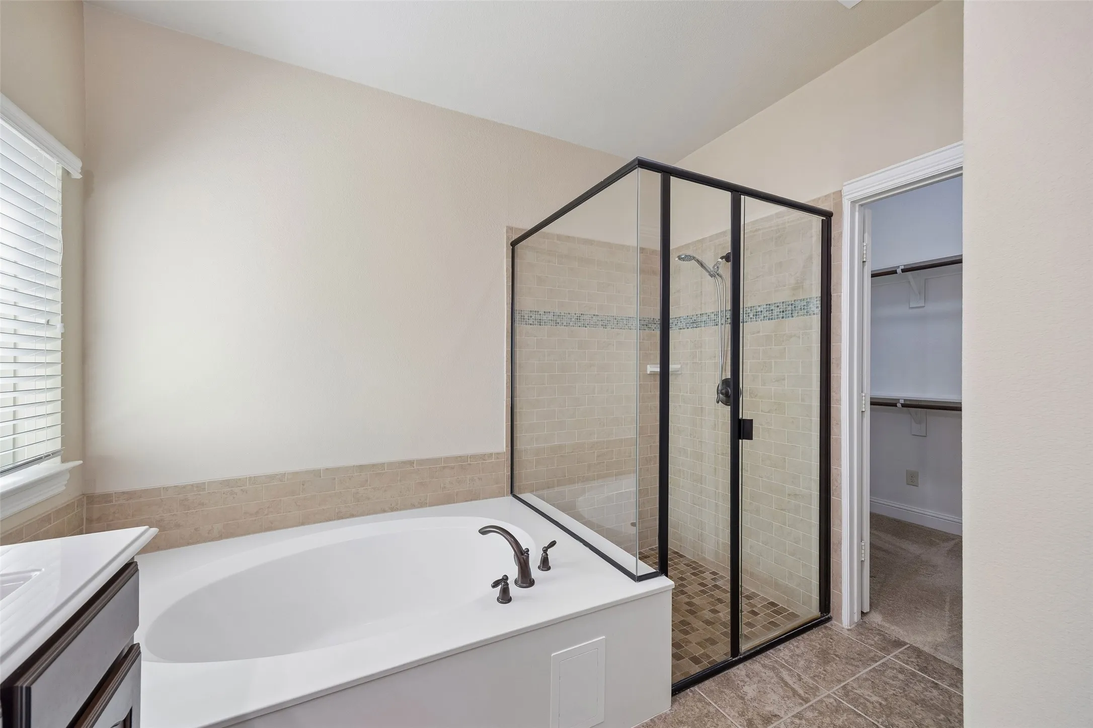 Soaking tub with bronze-finish fixtures, glass-enclosed shower with tiled walls and floor, and a built-in closet with shelving