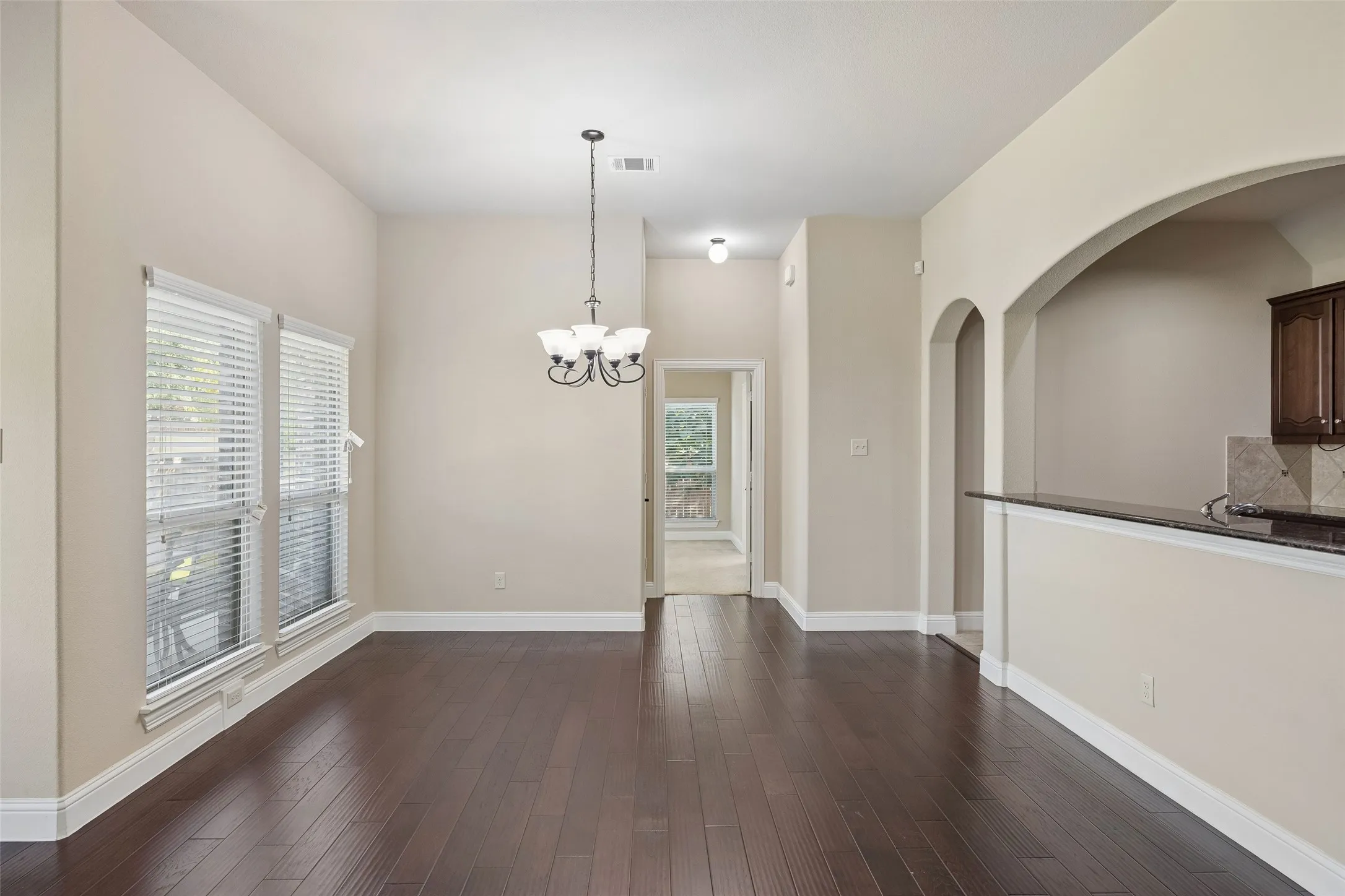 High ceilings, dark wood-finish flooring, two large windows with blinds, arched architectural elements
