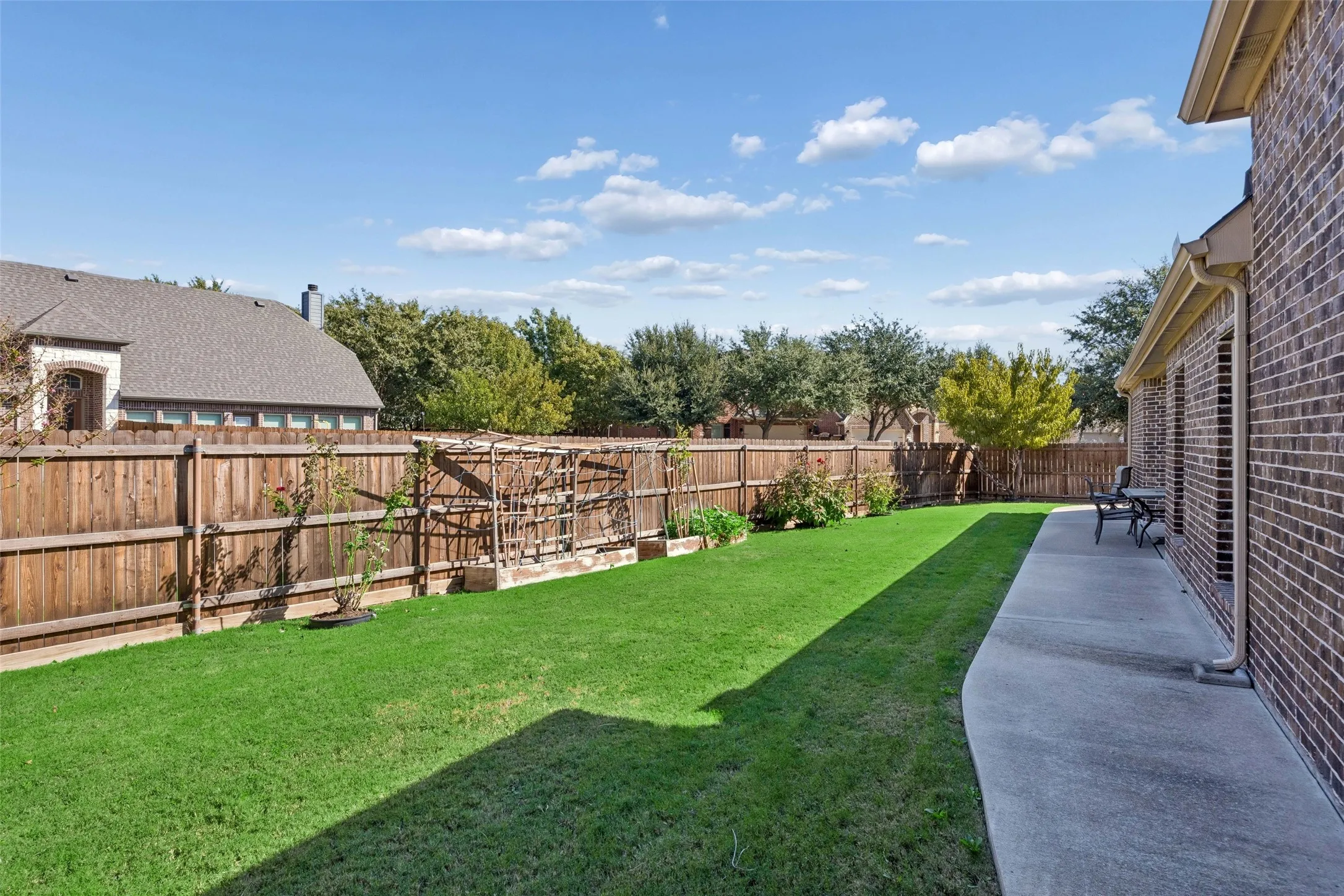 Expansive backyard featuring a manicured lawn, wood privacy fence, and concrete patio