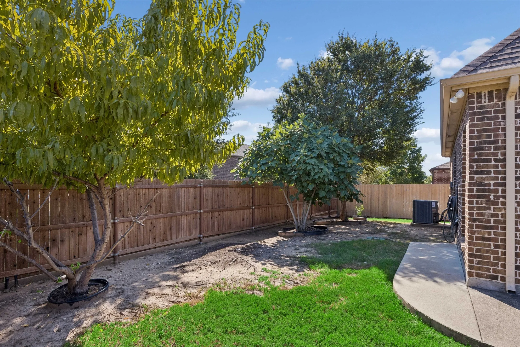 Fenced backyard with mature trees, a concrete pathway, and a brick exterior