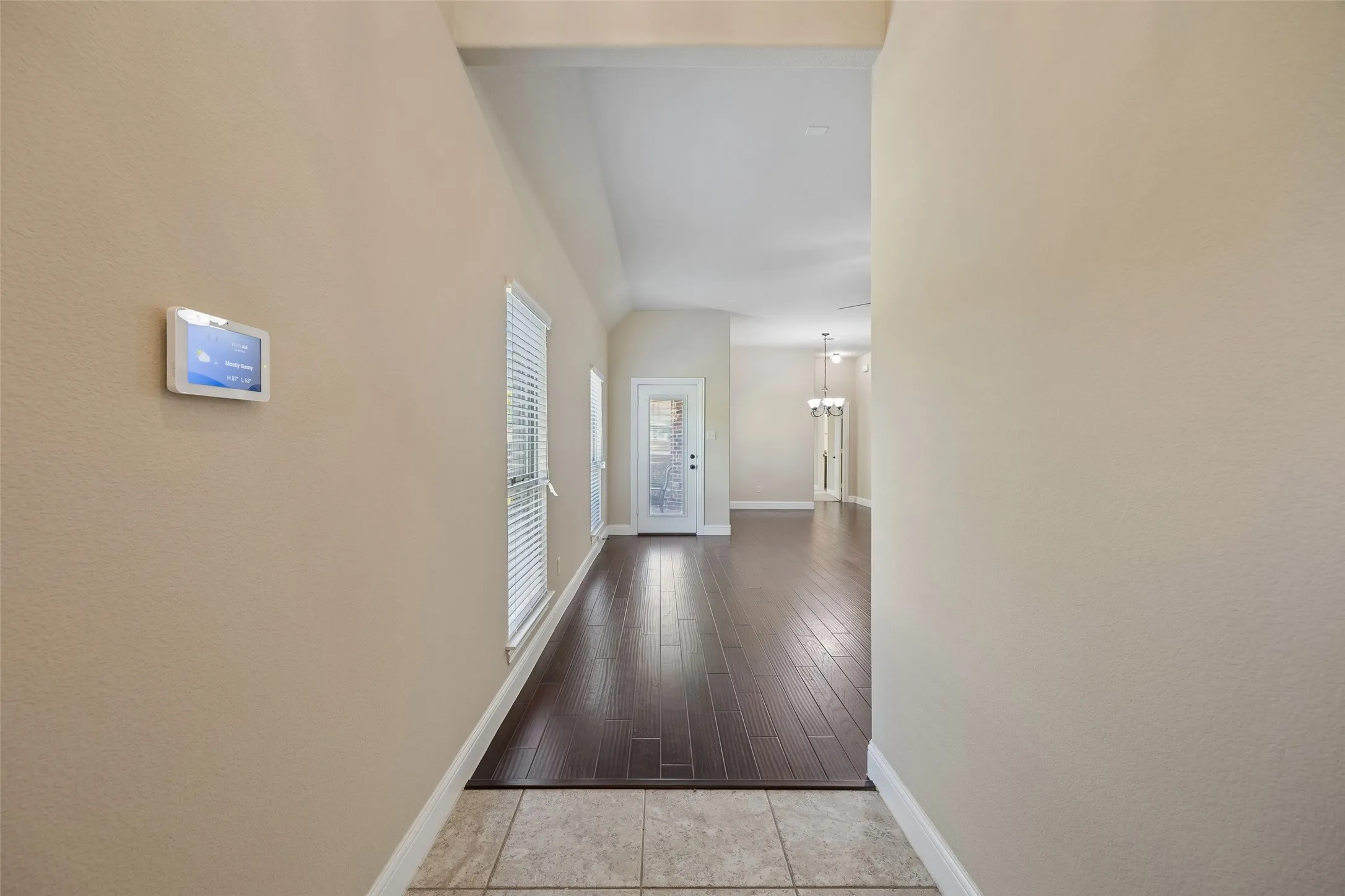 Tile flooring entryway with engineered wood-finish flooring extending into the main area, vaulted ceilings, and a smart thermostat