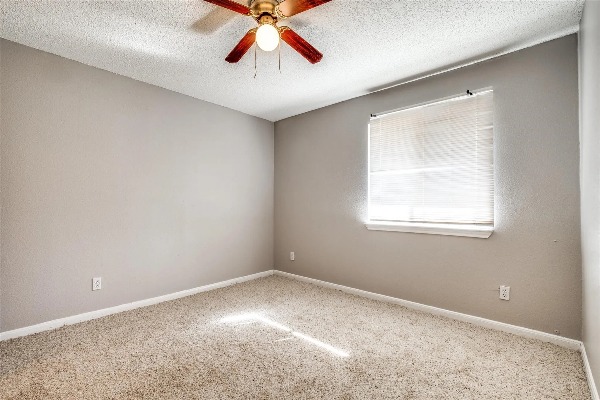 Neutral wall color, carpeted flooring, window with blinds, and a ceiling fan with integrated lighting
