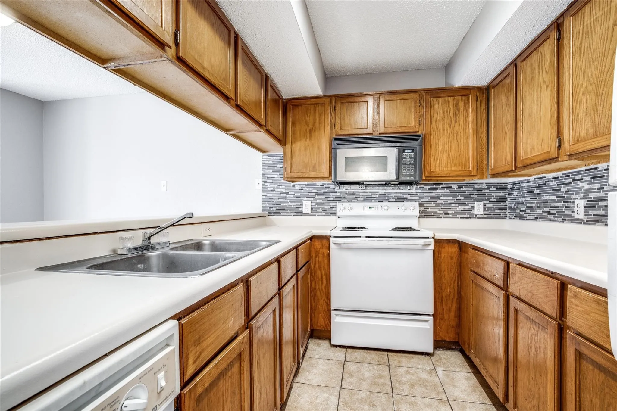 Kitchen featuring wood cabinetry, a dual basin stainless steel sink, tile backsplash, and integrated microwave
