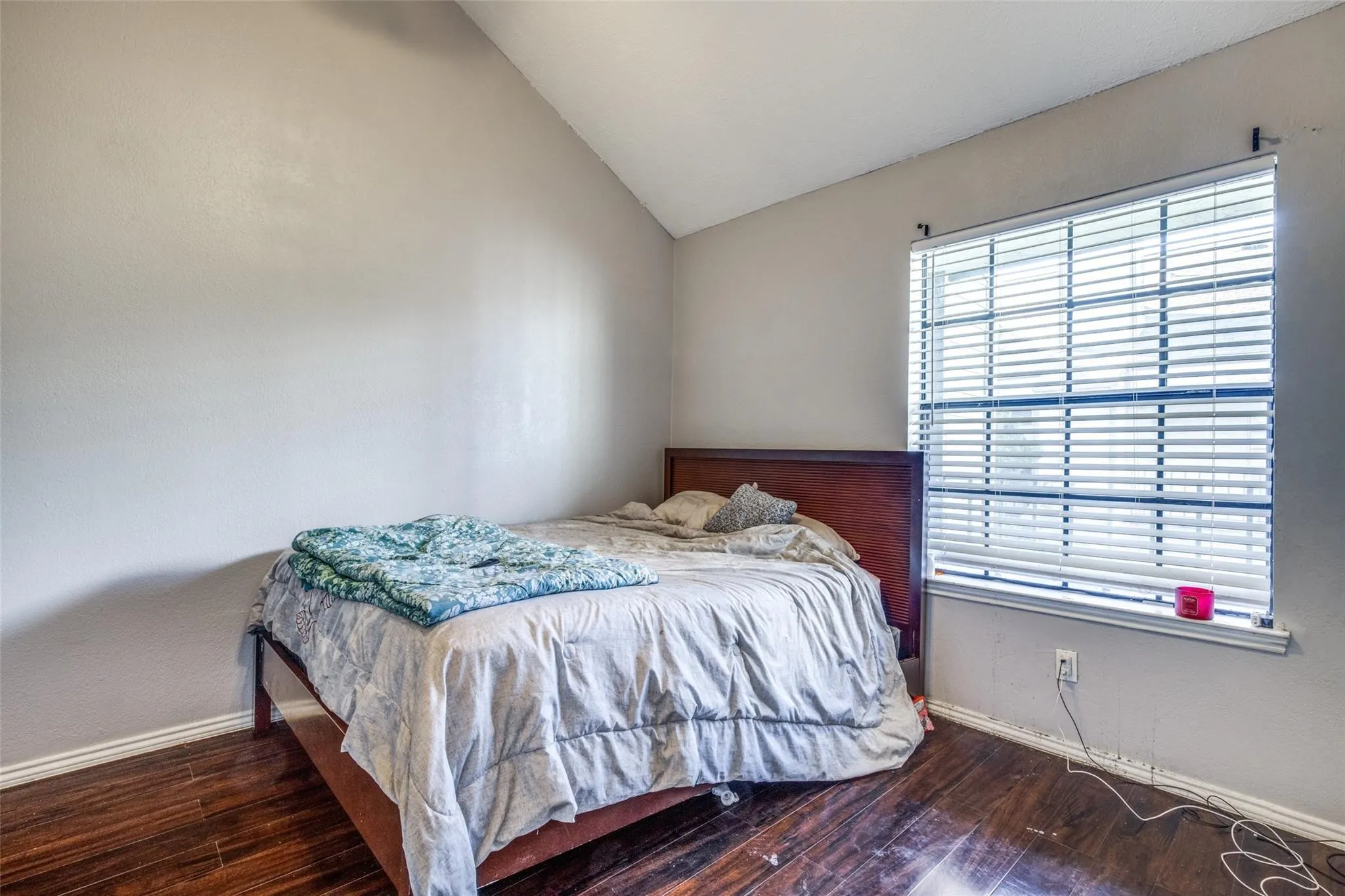 Vaulted ceiling, wood-finish flooring, and a large window with horizontal blinds