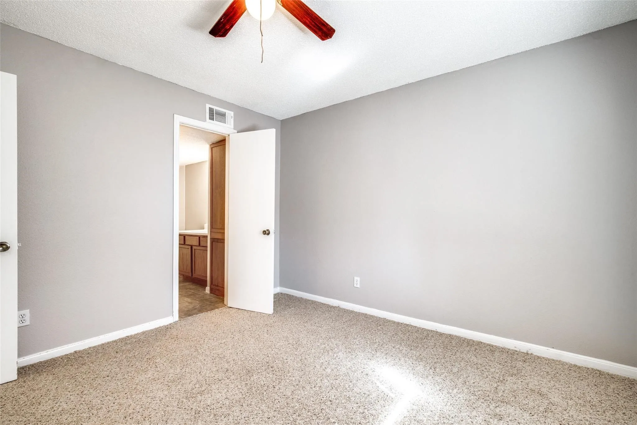 Carpeted flooring, neutral wall paint, ceiling fan, solid core door, wood-finish cabinetry