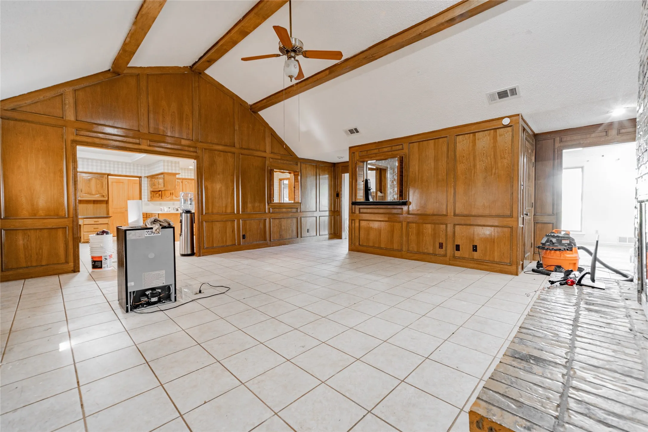 Vaulted ceiling with exposed wood beams, extensive wood paneling, tiled flooring, and a brick fireplace