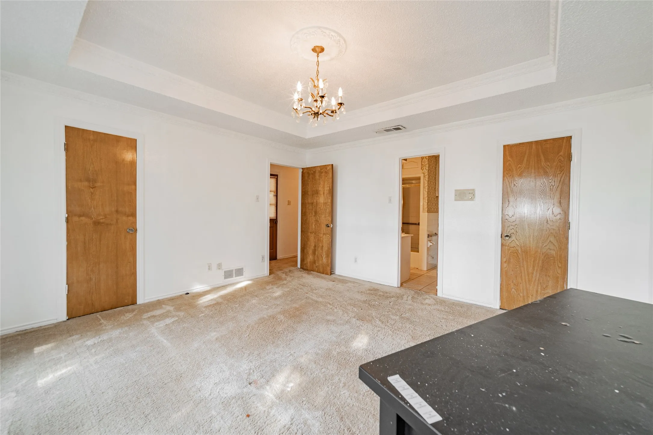 Tray ceiling with decorative molding, chandelier lighting, white walls, and wood-panel doors
