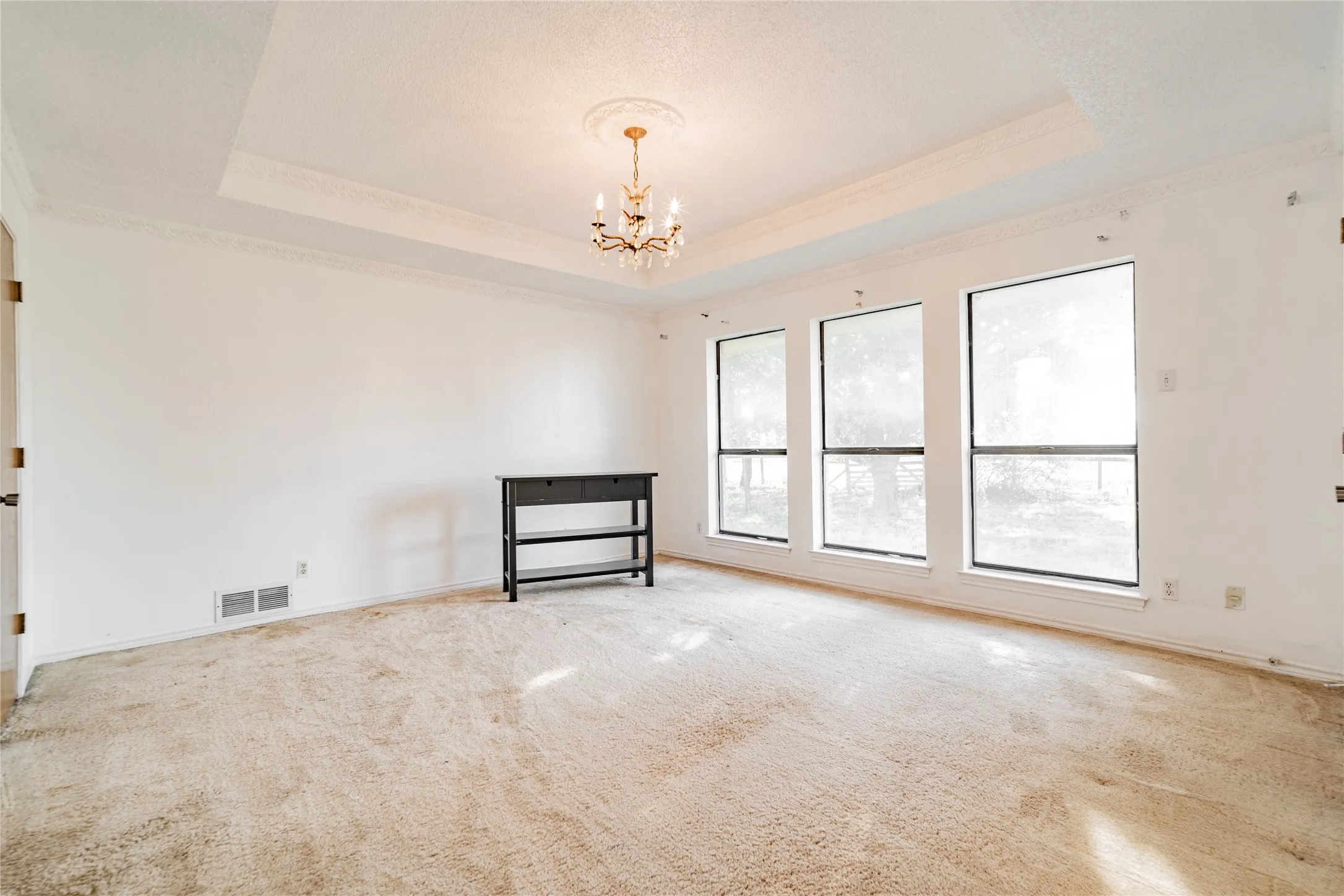 Tray ceiling with crown molding, decorative chandelier, and three large windows