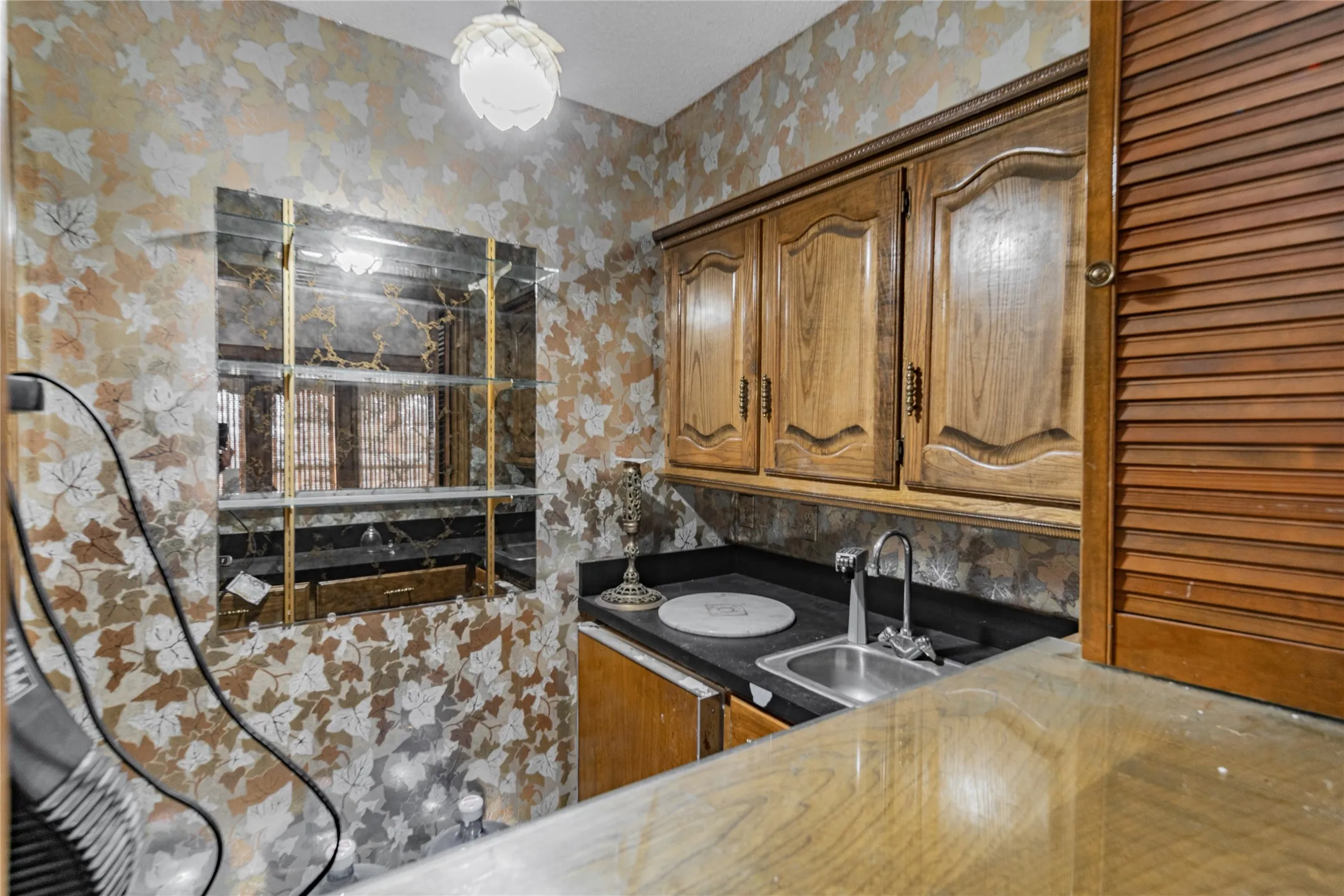 Built-in wet bar featuring wood cabinetry, a stainless steel sink, and dark countertops