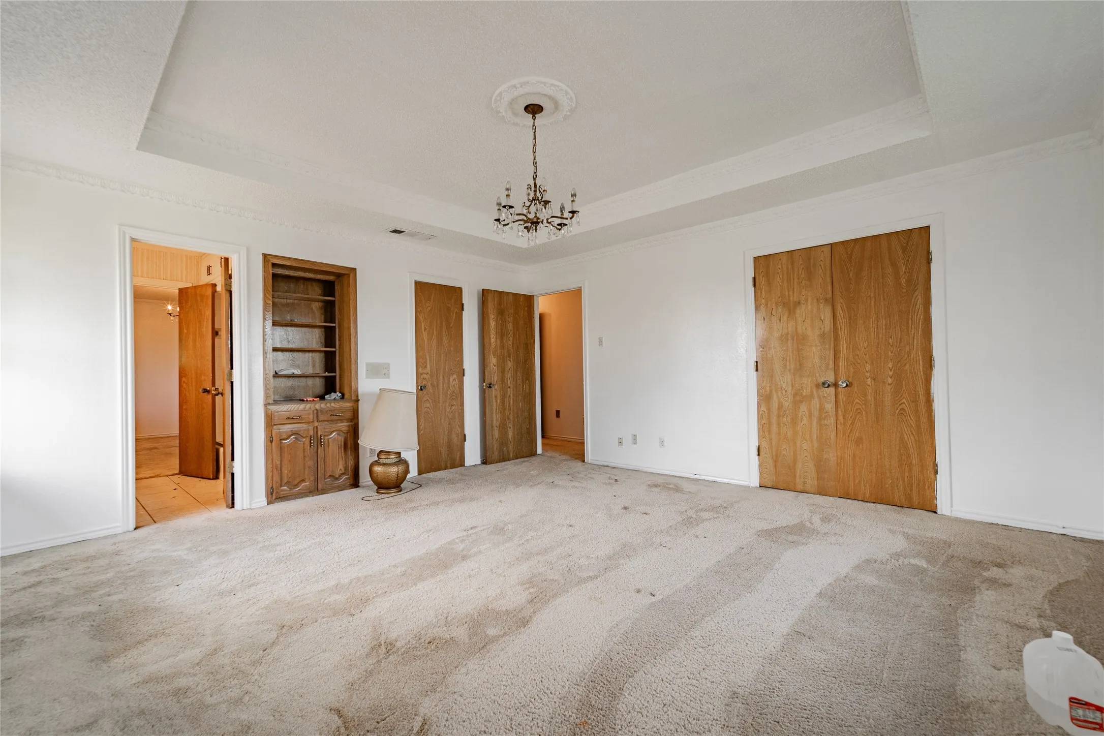 Tray ceiling with decorative molding, chandelier lighting, built-in shelving, and wood doors