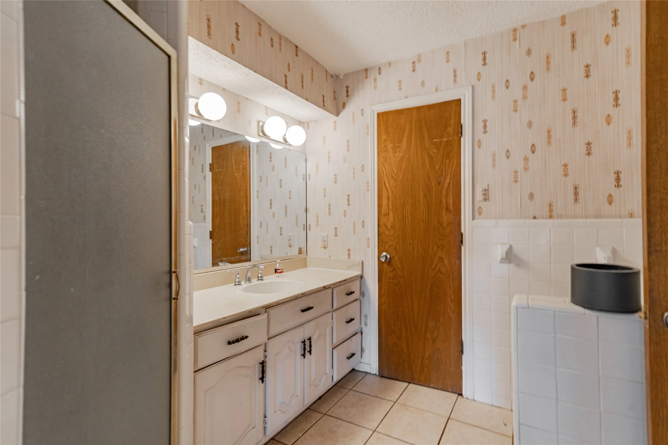 Single vanity with a white countertop and integrated sink, dual-door white cabinetry, and a three-bulb vanity light fixture