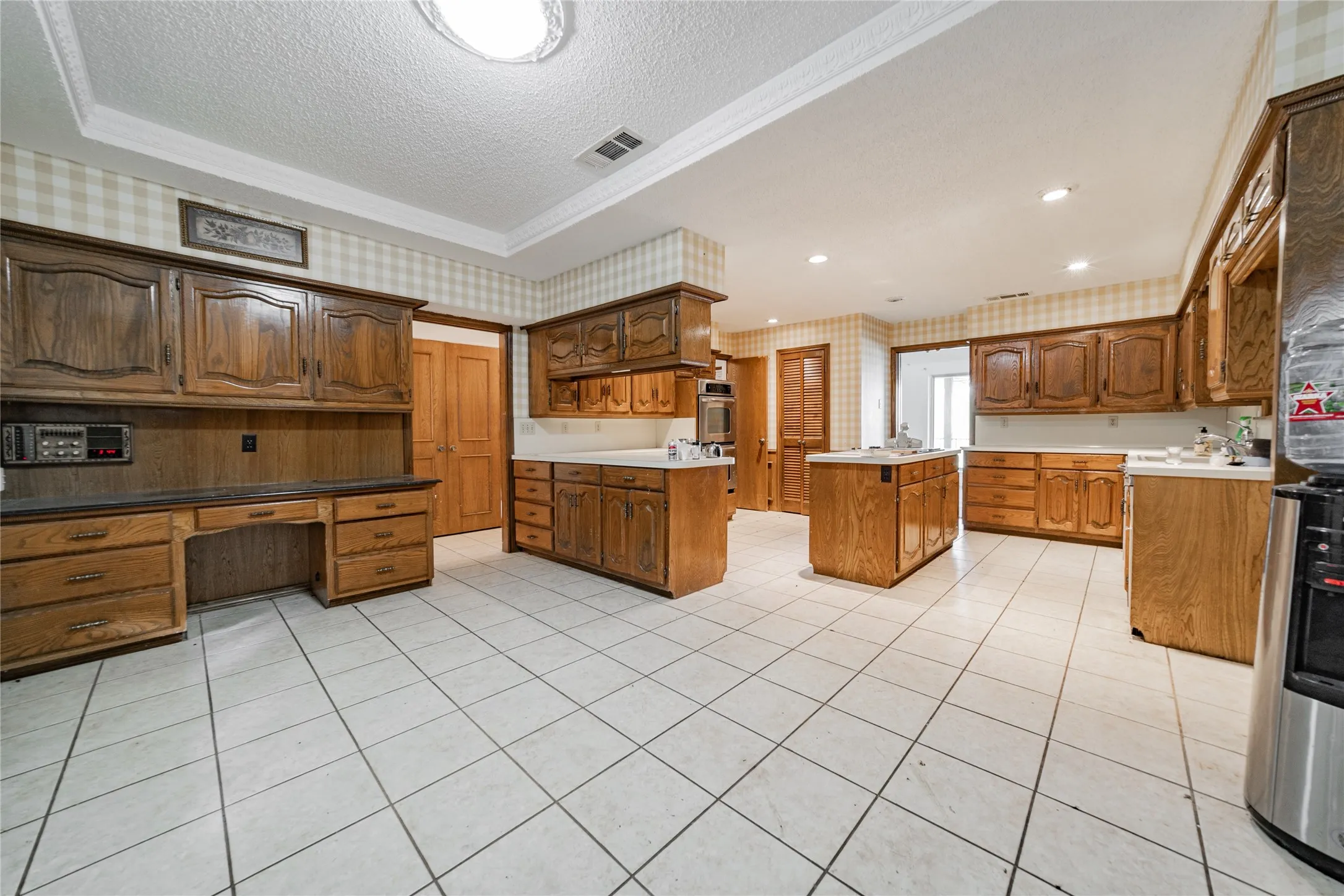 Kitchen featuring extensive wood cabinetry, white tile flooring, built-in desk area, and a central island