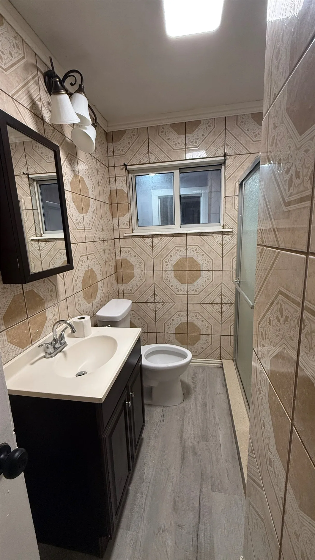 Bathroom featuring patterned wall tiling, a vanity with a dark wood-finish cabinet, a white sink, and light wood-finish flooring