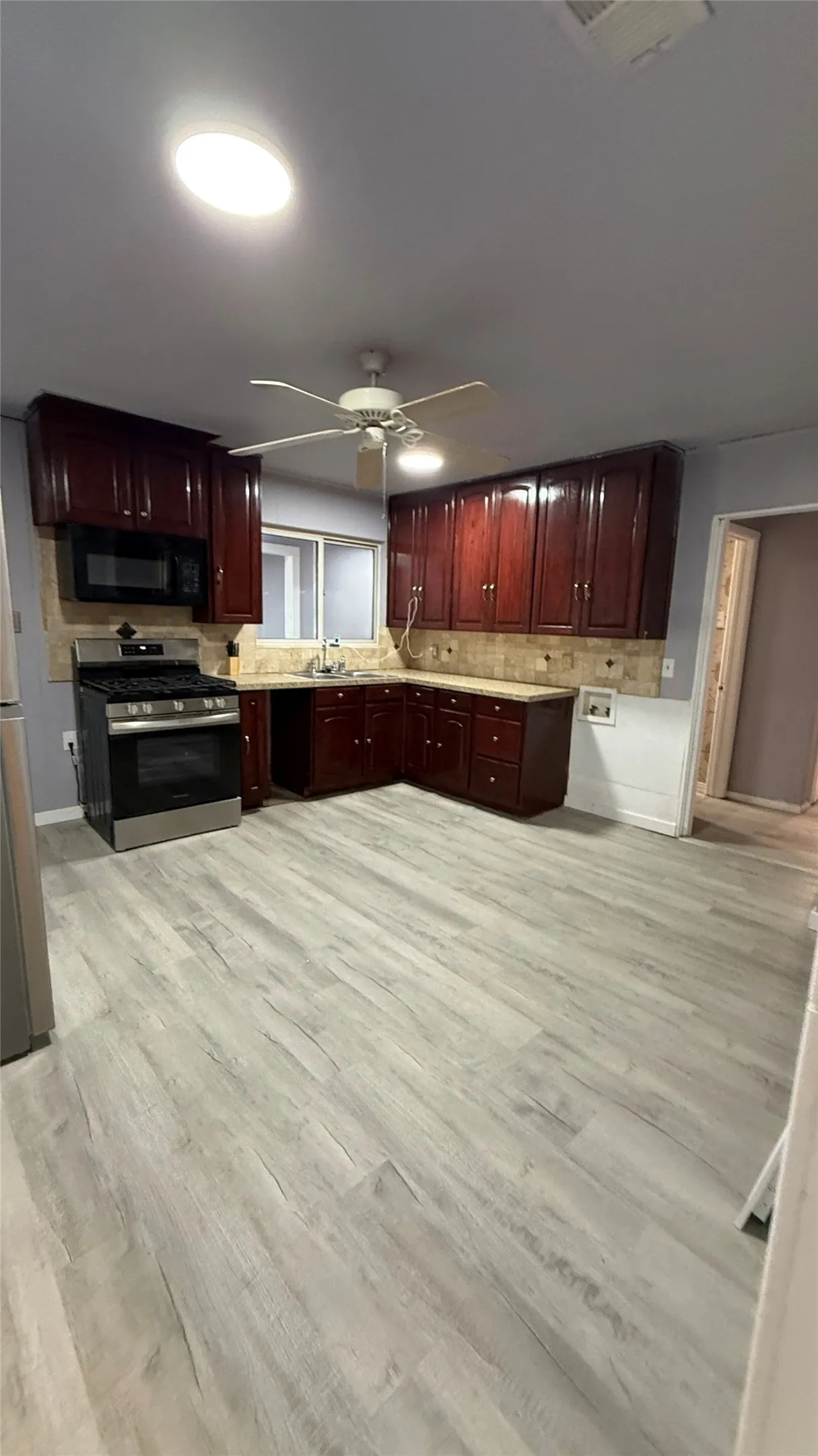 Kitchen featuring wood-finish flooring, dark wood cabinetry, stainless steel oven, and a tiled backsplash