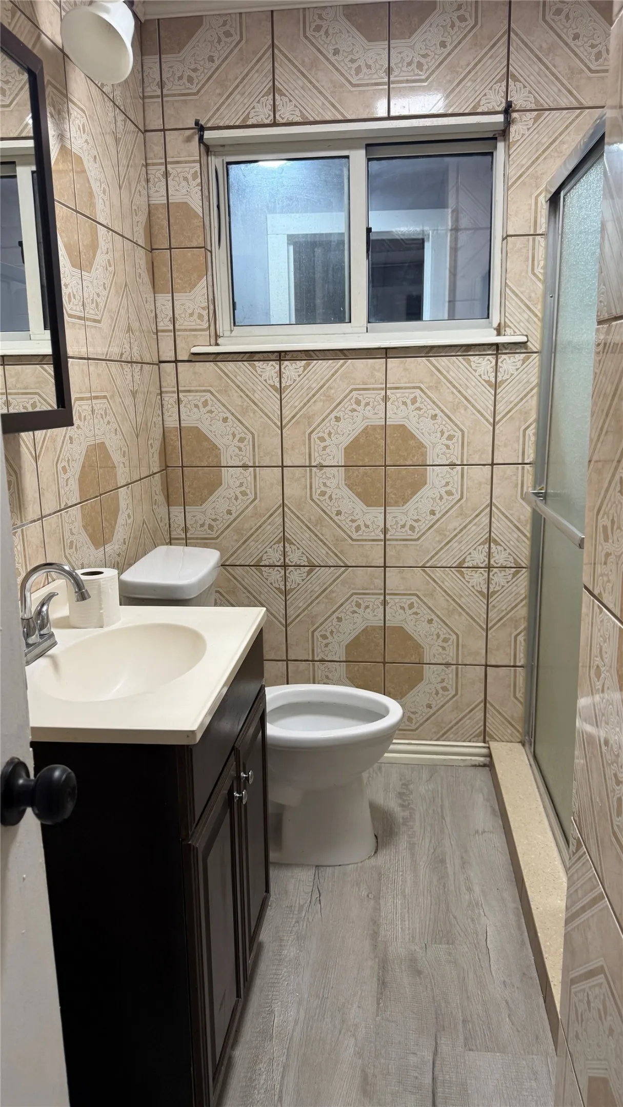 Patterned wall tiling, a single vanity with storage, a white toilet, and wood-finish flooring