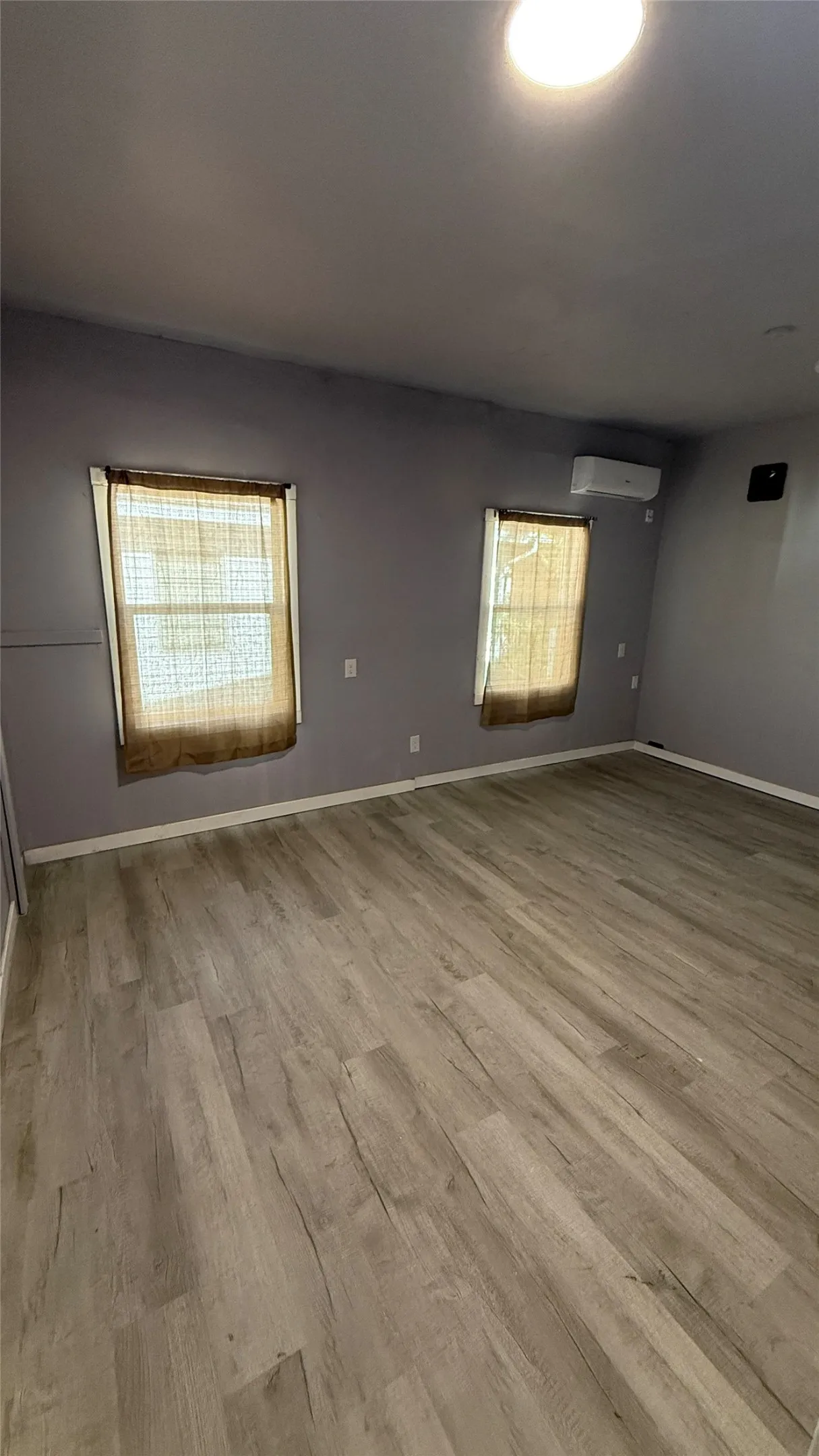 Light wood-finish flooring, two windows, and a wall-mounted climate control unit