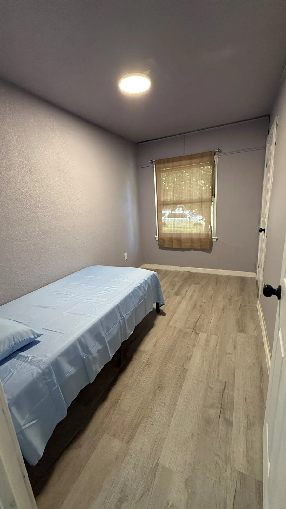 Recessed ceiling light, wood-finish flooring, single window with blinds, white paneled door