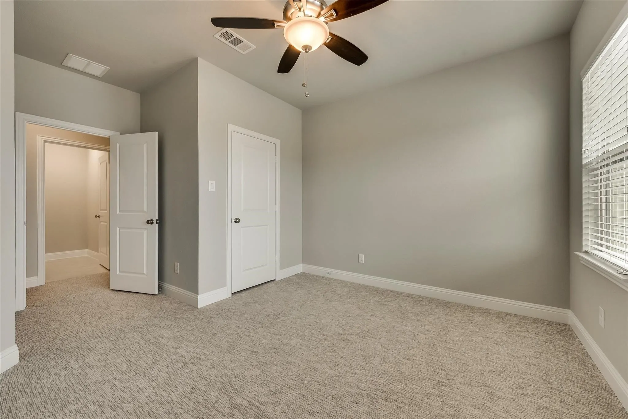 Plush patterned carpeting, ceiling fan with integrated lighting, window with horizontal blinds, and paneled interior doors