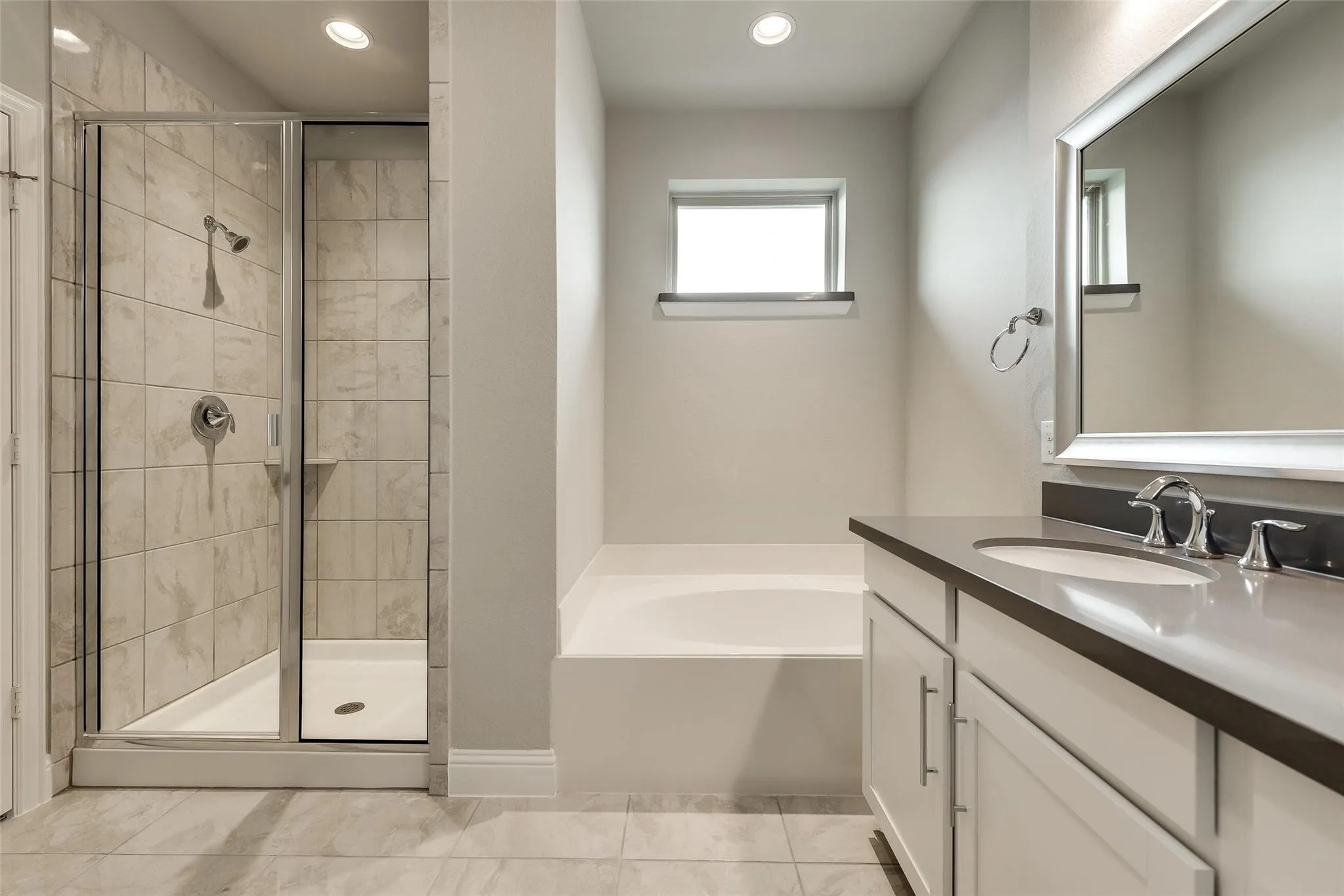 Shower with glass enclosure, separate soaking tub, double vanity with integrated sinks, framed mirror, and tiled flooring