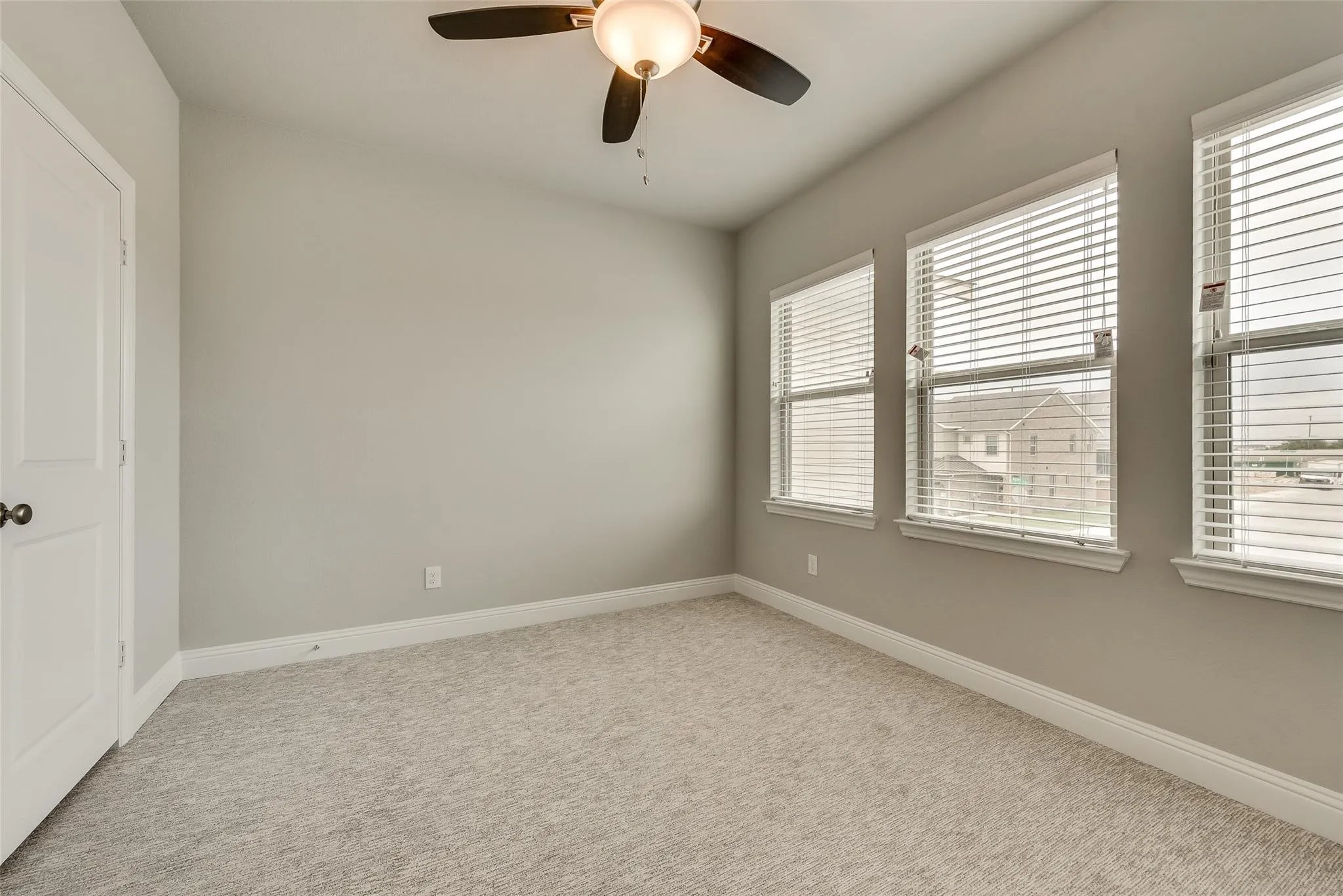 Recessed panel door with dark hardware, three windows with blinds, ceiling fan with integrated lighting, and carpeted flooring