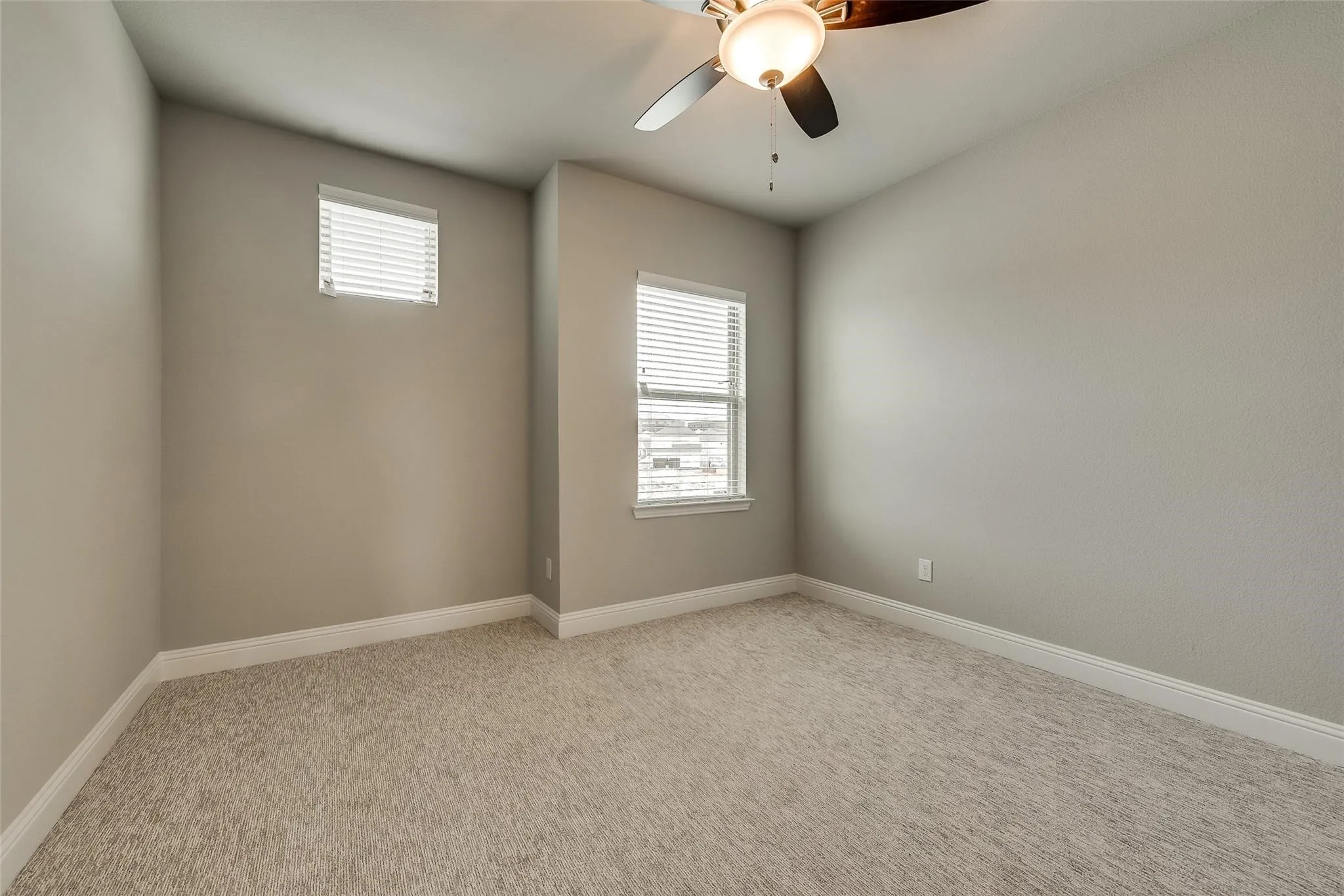 Bright secondary bedroom featuring neutral painted walls, plush carpeting, dual windows with plantation shutters, and ceiling fan with integrated lighting