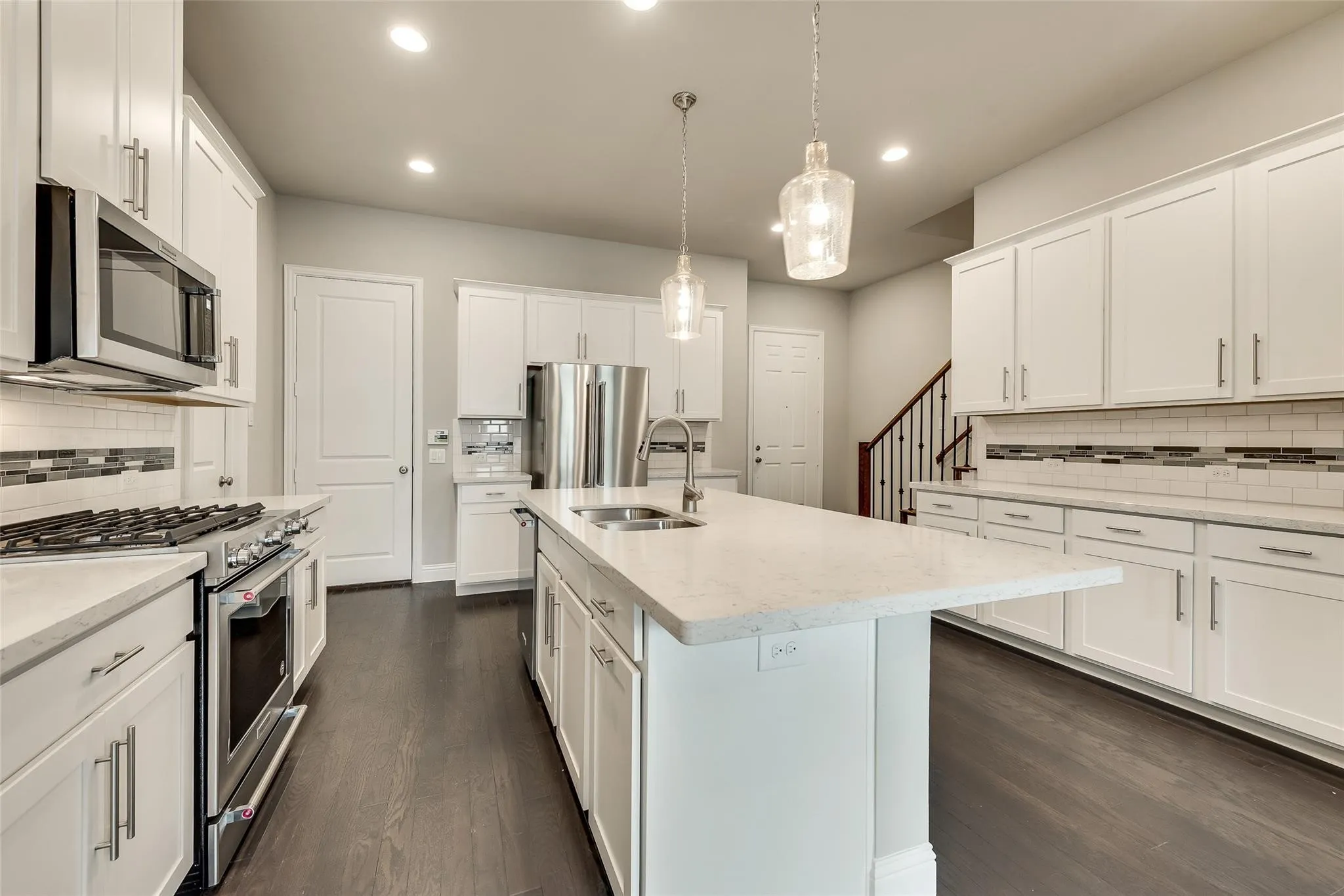 Kitchen featuring white cabinetry, stainless steel appliances, a center island with sink, pendant lighting, and wood-finish flooring